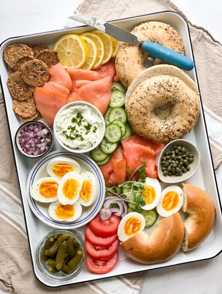 Bagel brunch board with smoked salmon, eggs, cucumbers, capers, cream cheese, and bagels.