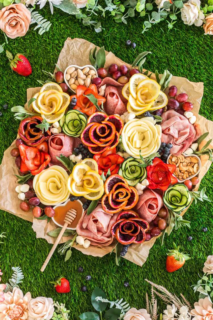 Charcuterie board styled as a bouquet with meats, cheeses, fruits, nuts, and floral garnishes.