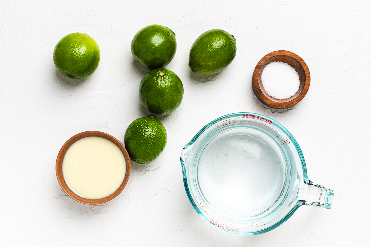Ingredients for Brazilian lemonade: fresh limes, condensed milk, sugar, and water, pin shows simple lime drink recipe.