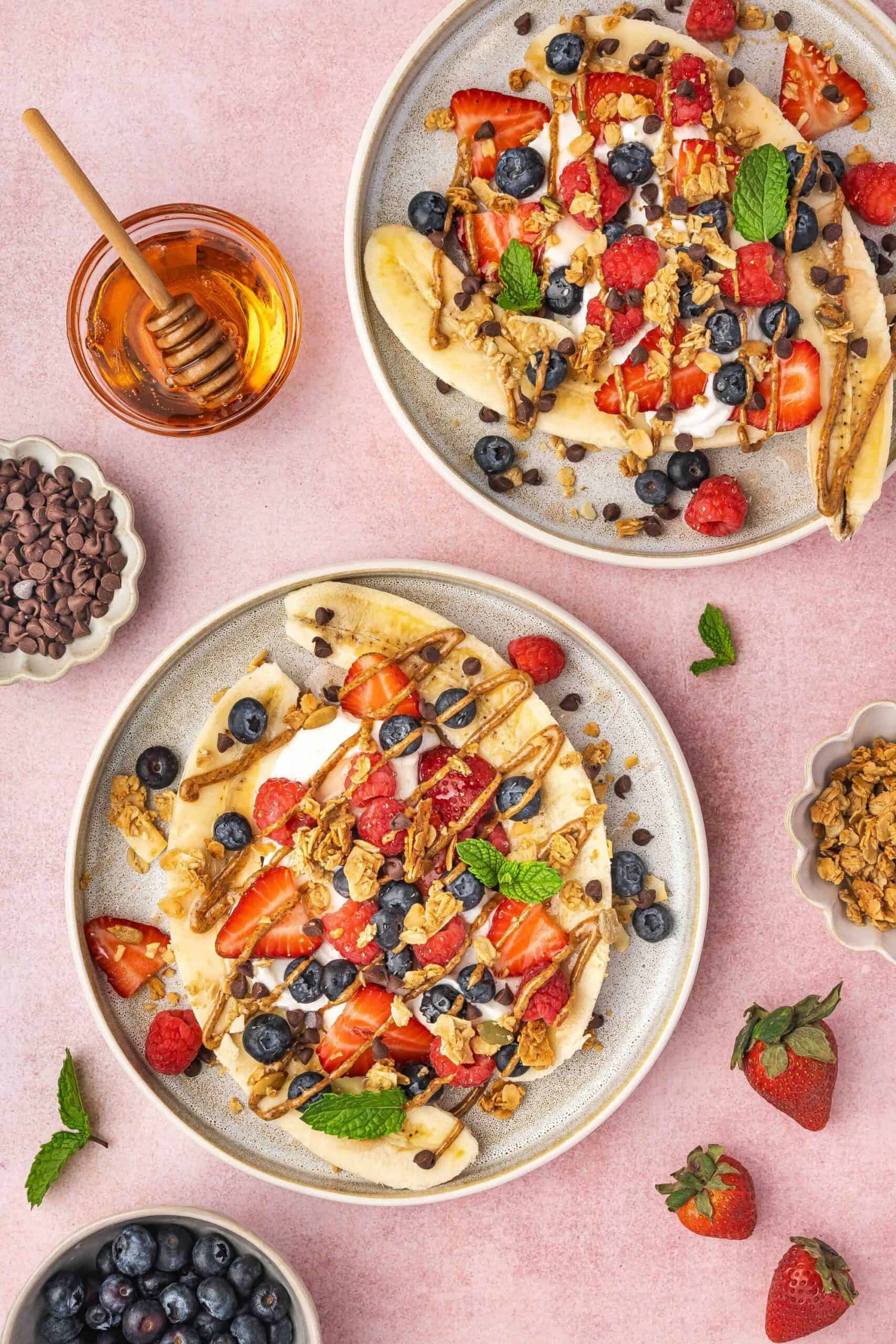 Banana split yogurt bowls topped with berries, granola, chocolate chips, and peanut butter drizzle.