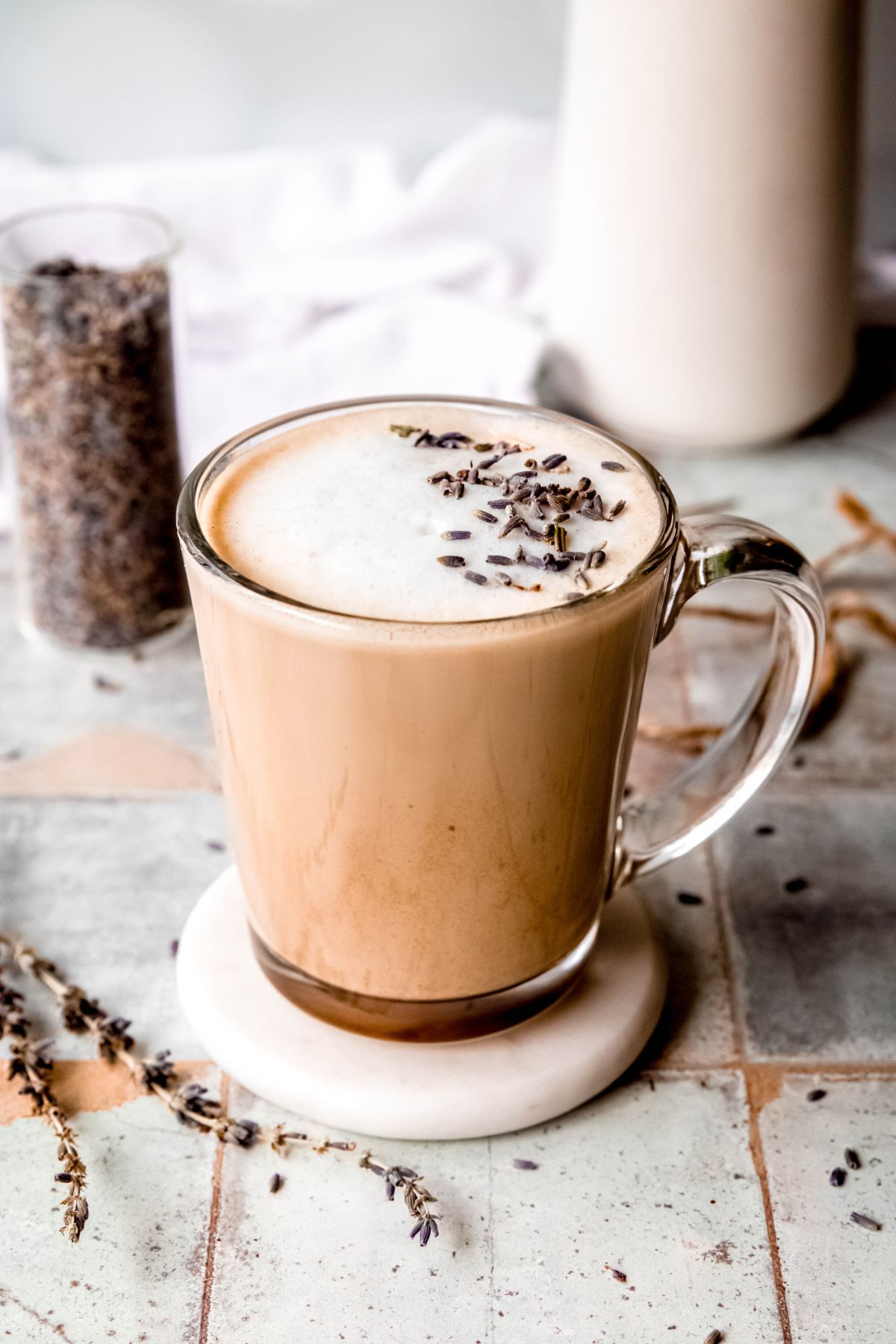 Hot lavender latte in a glass mug topped with foam and dried lavender buds.