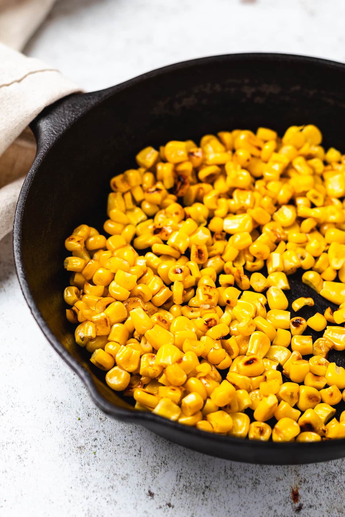 Cast iron skillet filled with roasted corn kernels on a light surface.