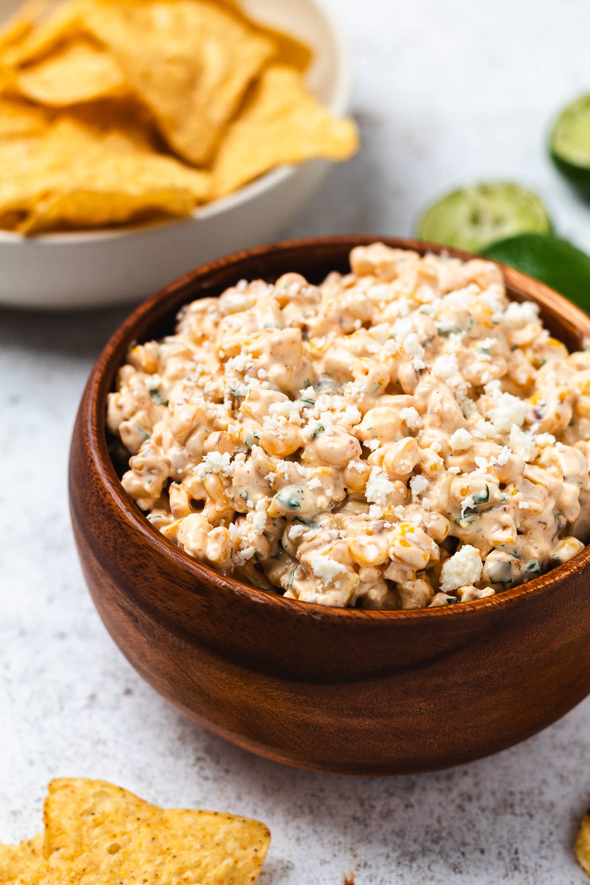Wooden bowl of creamy corn dip with chips and lime halves in the background.