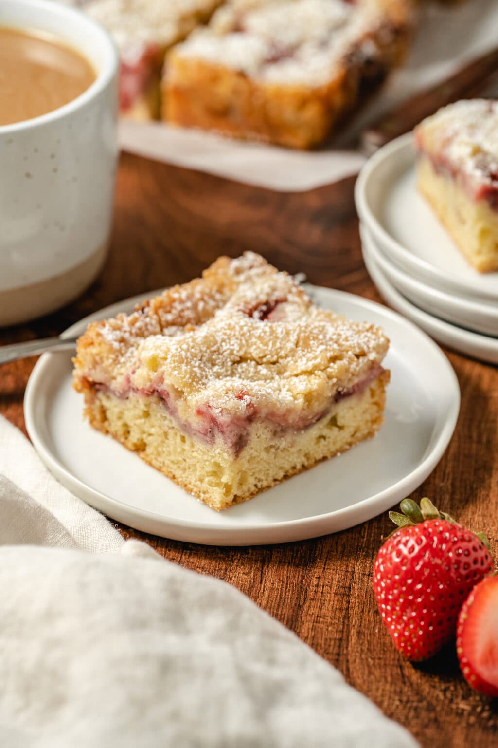Strawberry coffee cake slice dusted with powdered sugar on a plate with fresh strawberries.