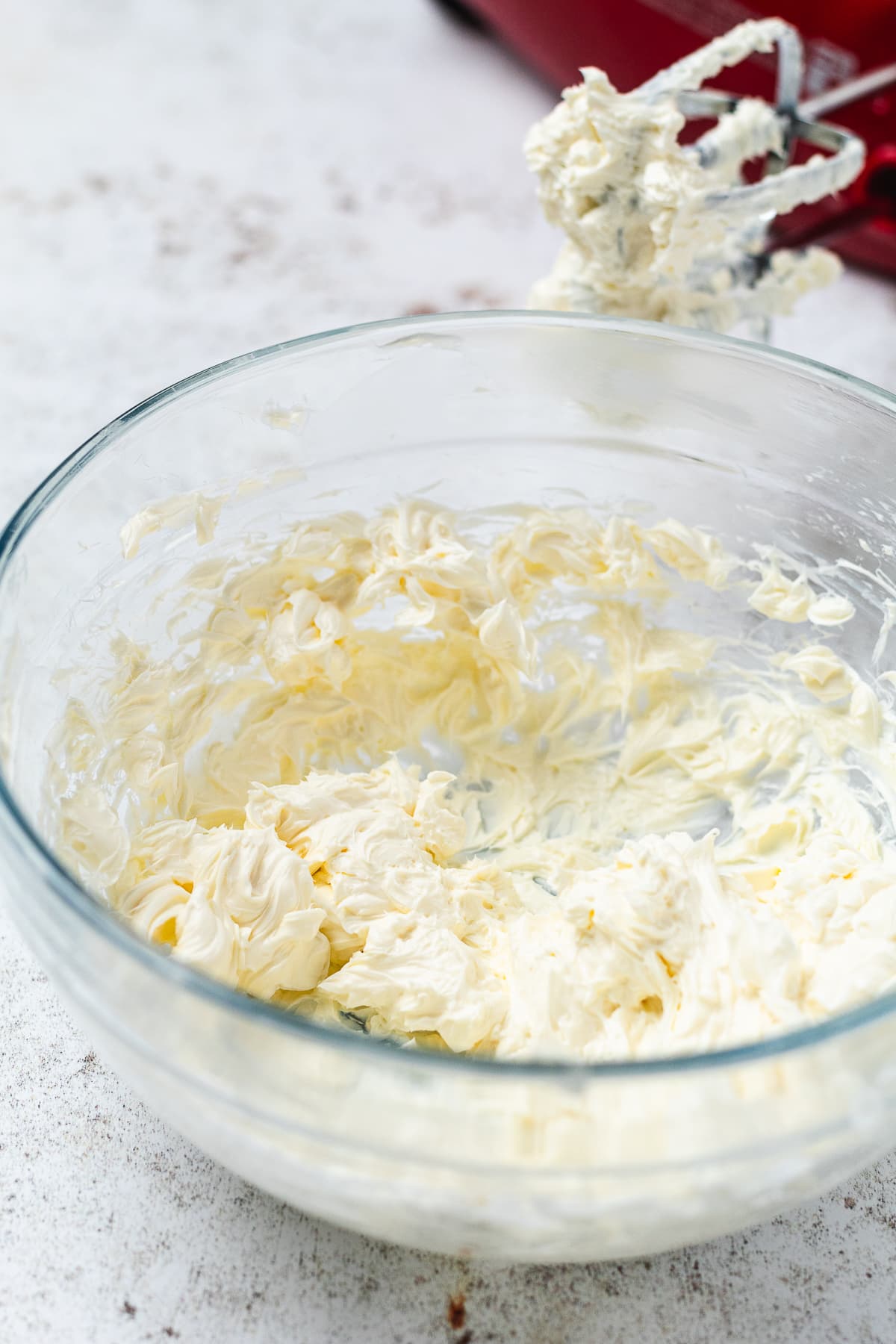 Glass bowl of whipped creamy mixture with a red stand mixer and coated beaters in the background.