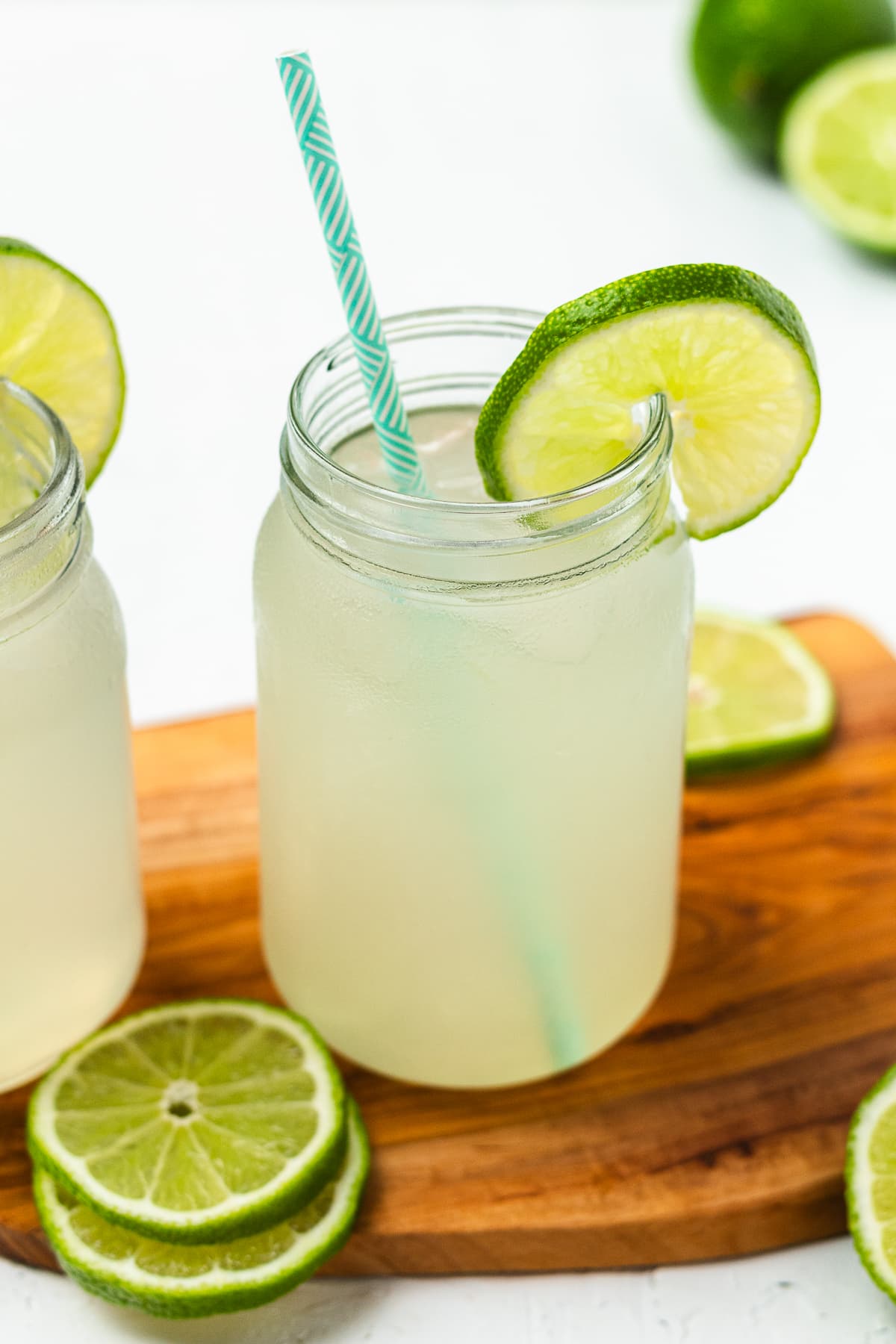 Mason jar of homemade limeade with lime garnish and straw, served on wooden board.