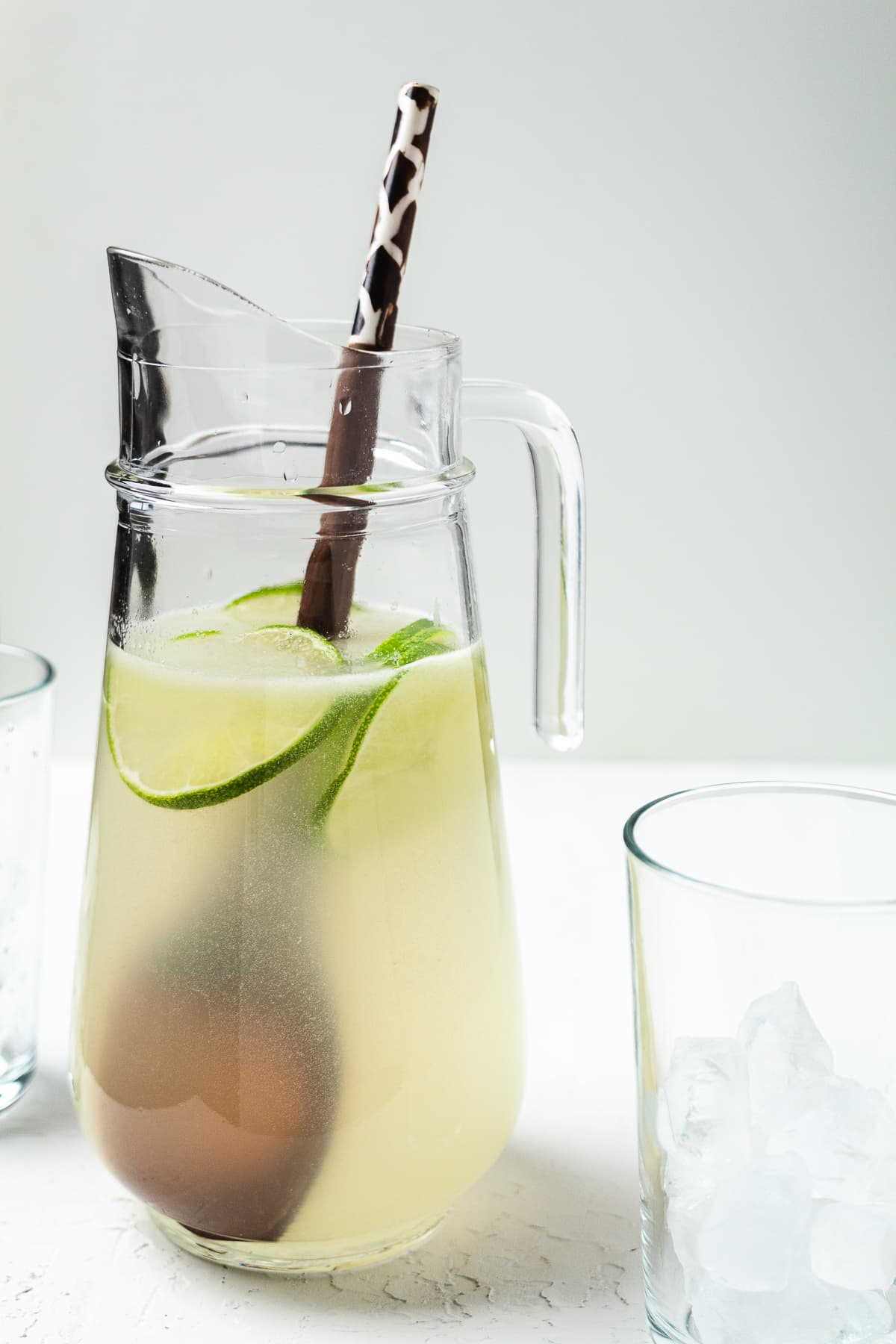 Pitcher of homemade limeade with lime slices and a stirring spoon, served with ice-filled glasses.