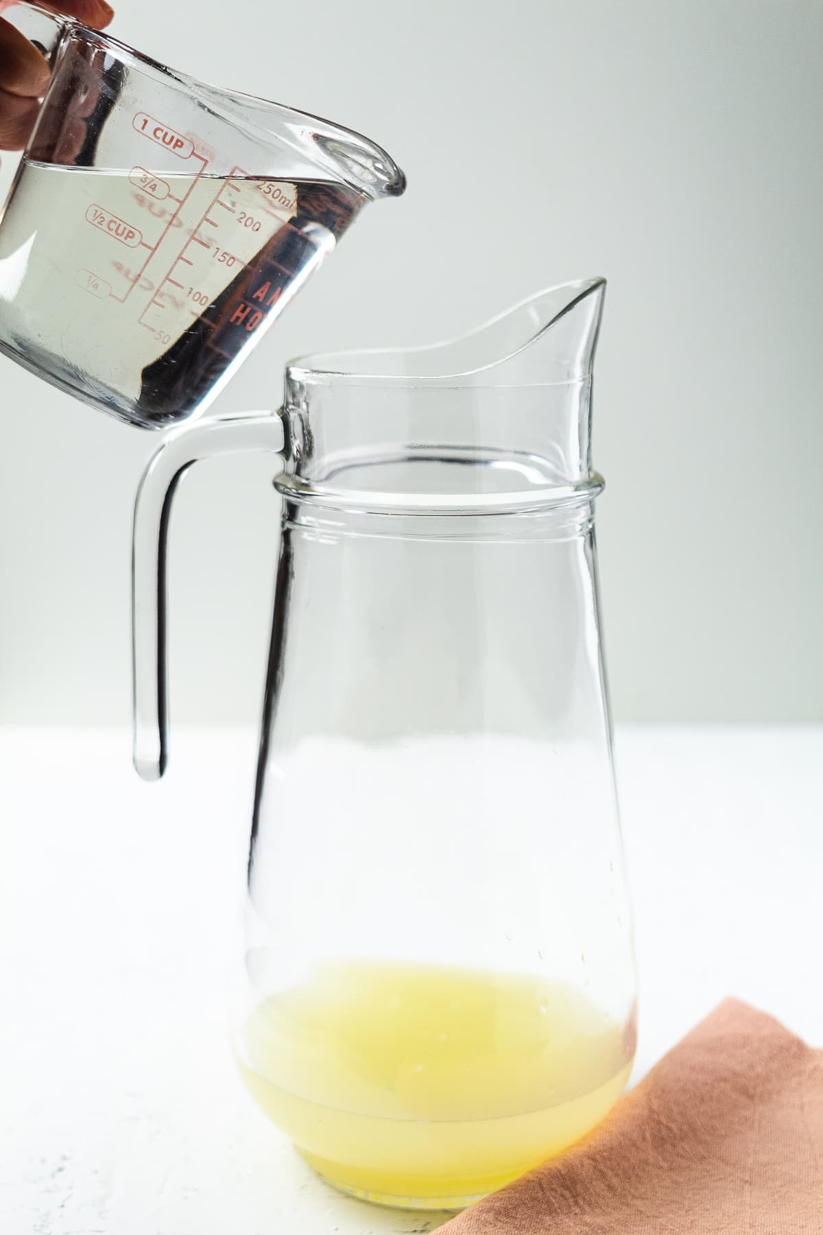 Pouring simple syrup into pitcher with fresh lime juice to make homemade limeade.