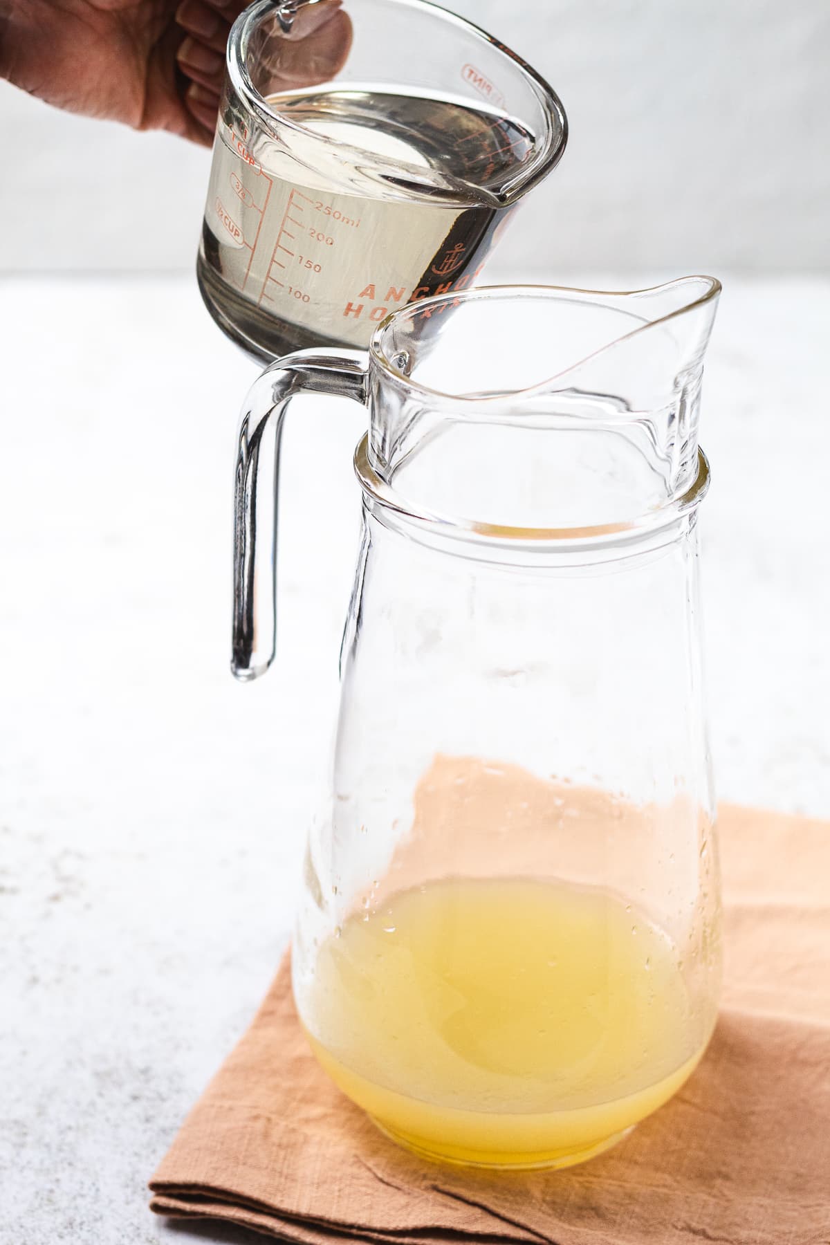 Pouring simple syrup into pitcher with lemon juice to make fresh lemonade.
