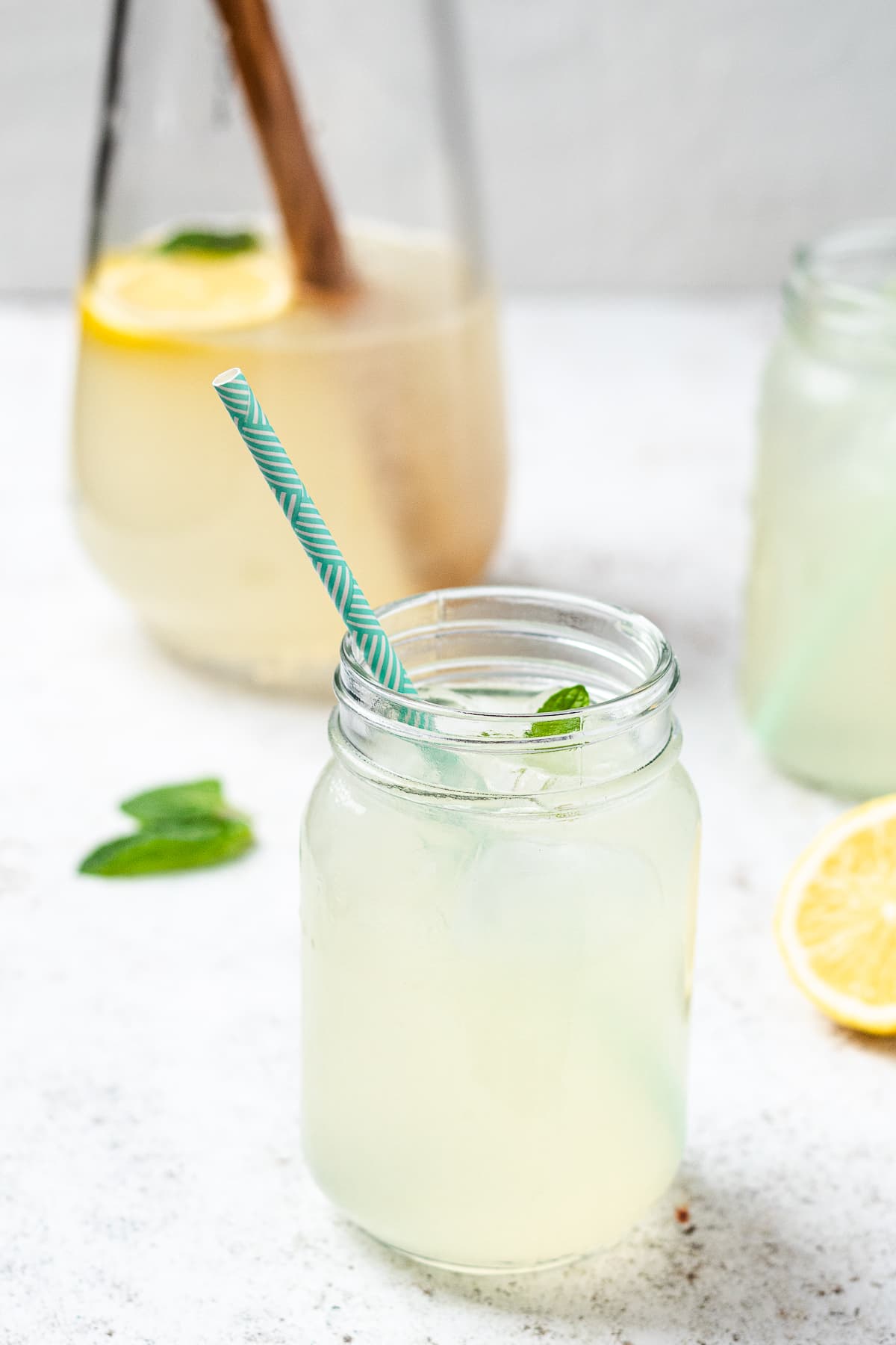 Mason jar of lemonade with ice and mint, lemon slice nearby on light surface.