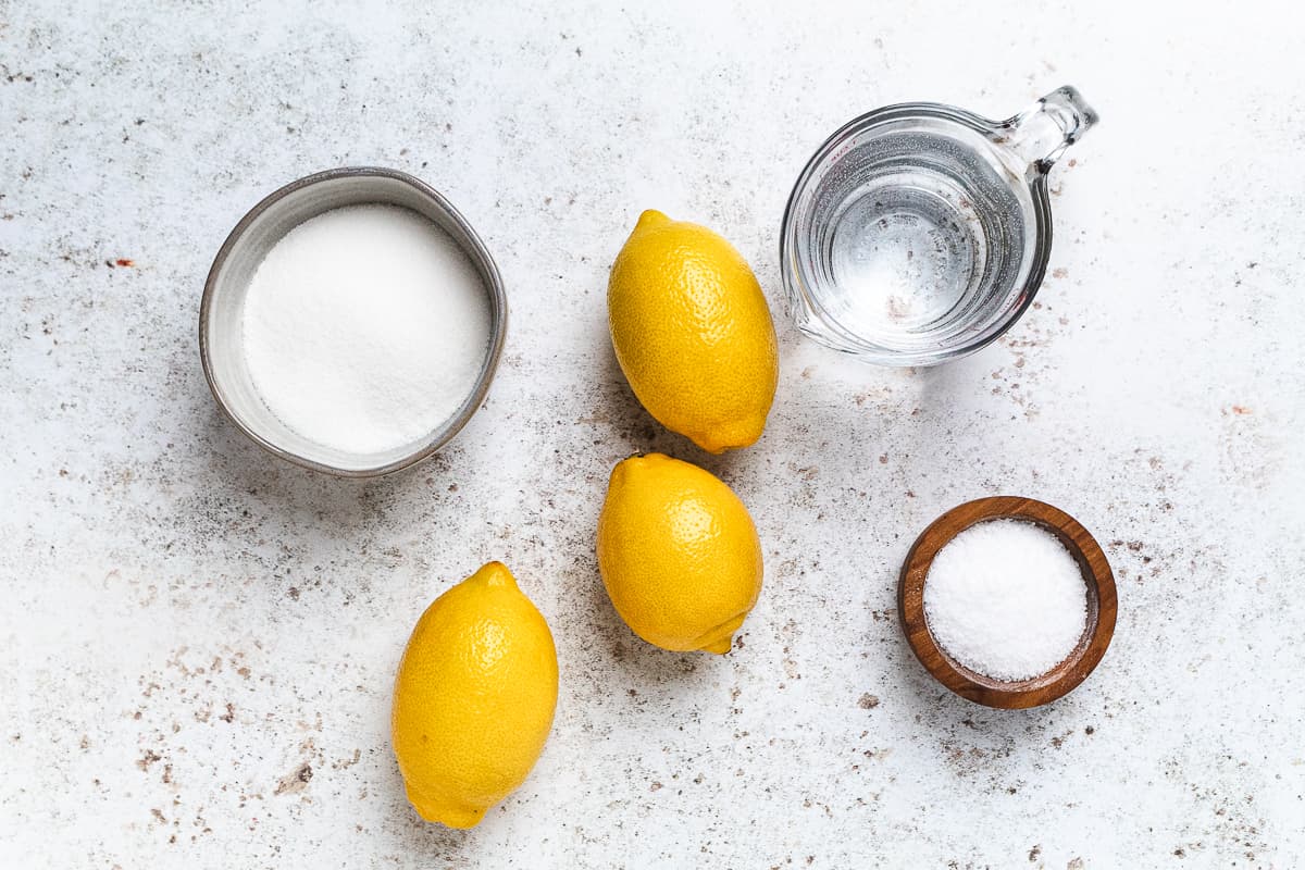 Ingredients for fresh lemonade: lemons, sugar, water, and salt on neutral surface.