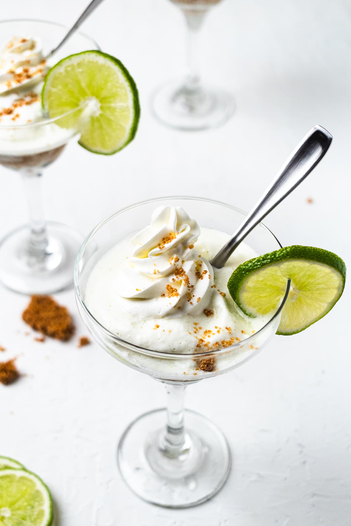 Frozen key limeade in glass with whipped topping and lime slice, pin shows creamy lime drink recipe.