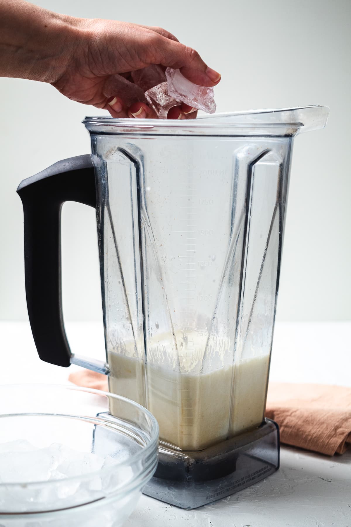 Hand adding ice cubes into blender with lemonade mixture for frozen lemonade.