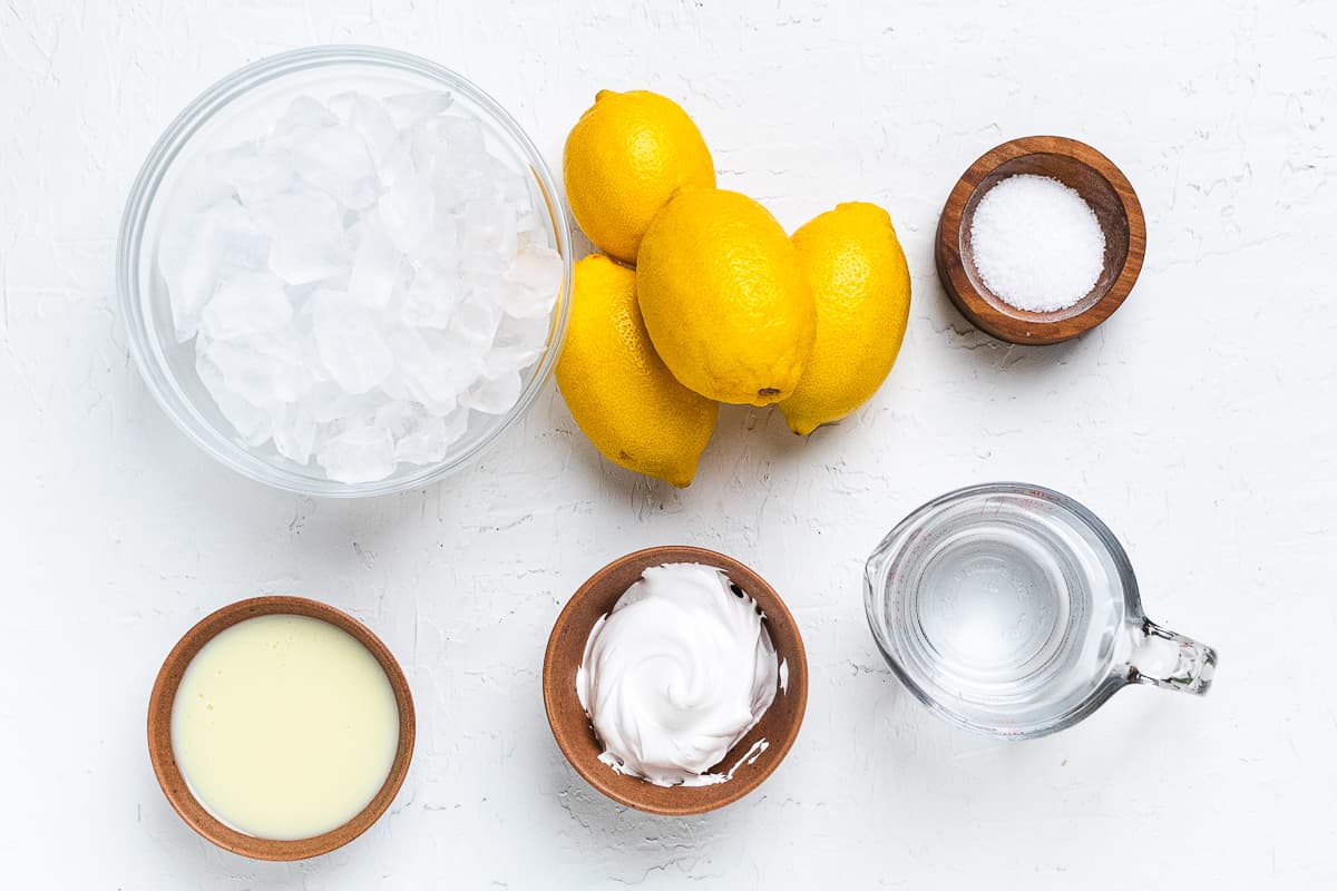 Ingredients for frozen lemon lemonade: lemons, sugar, ice, water, and whipped topping arranged overhead.