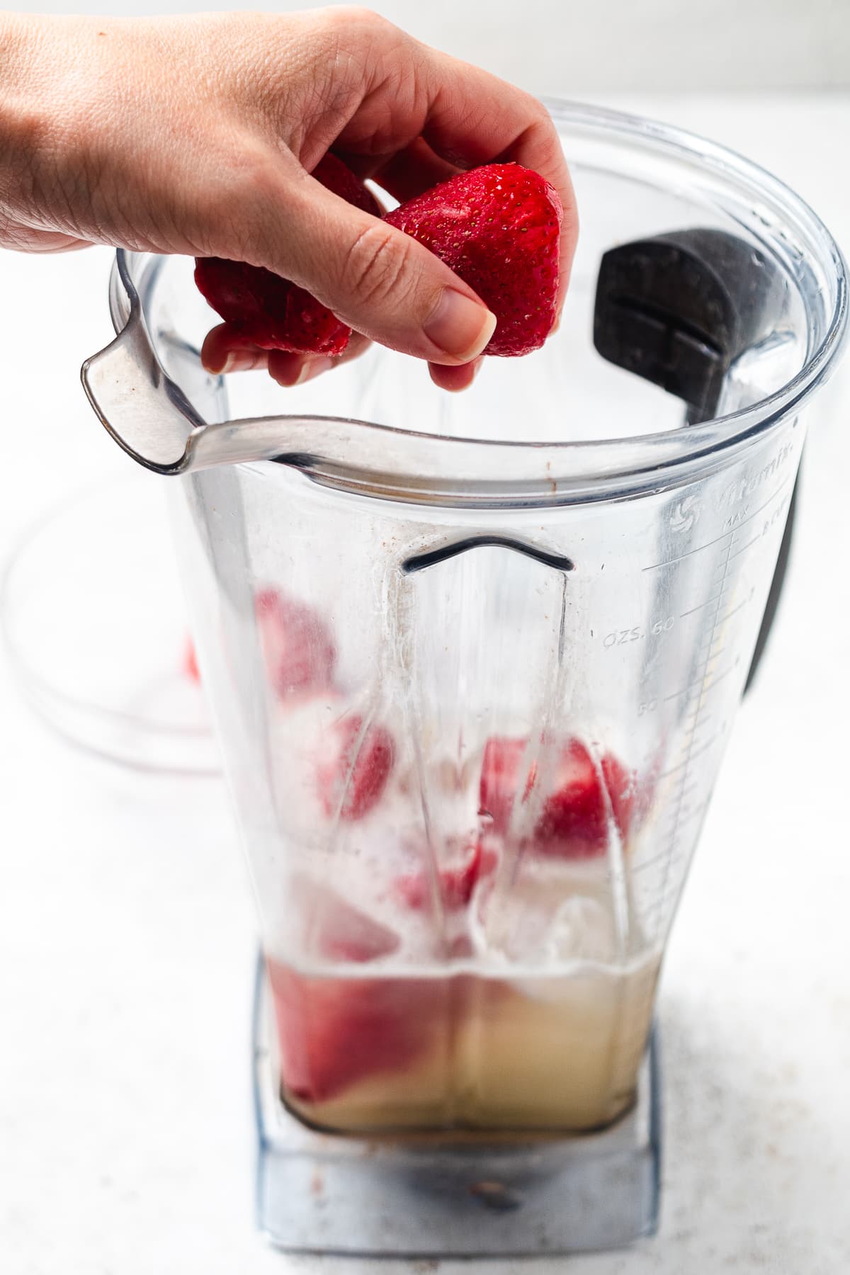 Hand adding strawberries to blender with lemonade base for frozen strawberry lemonade.