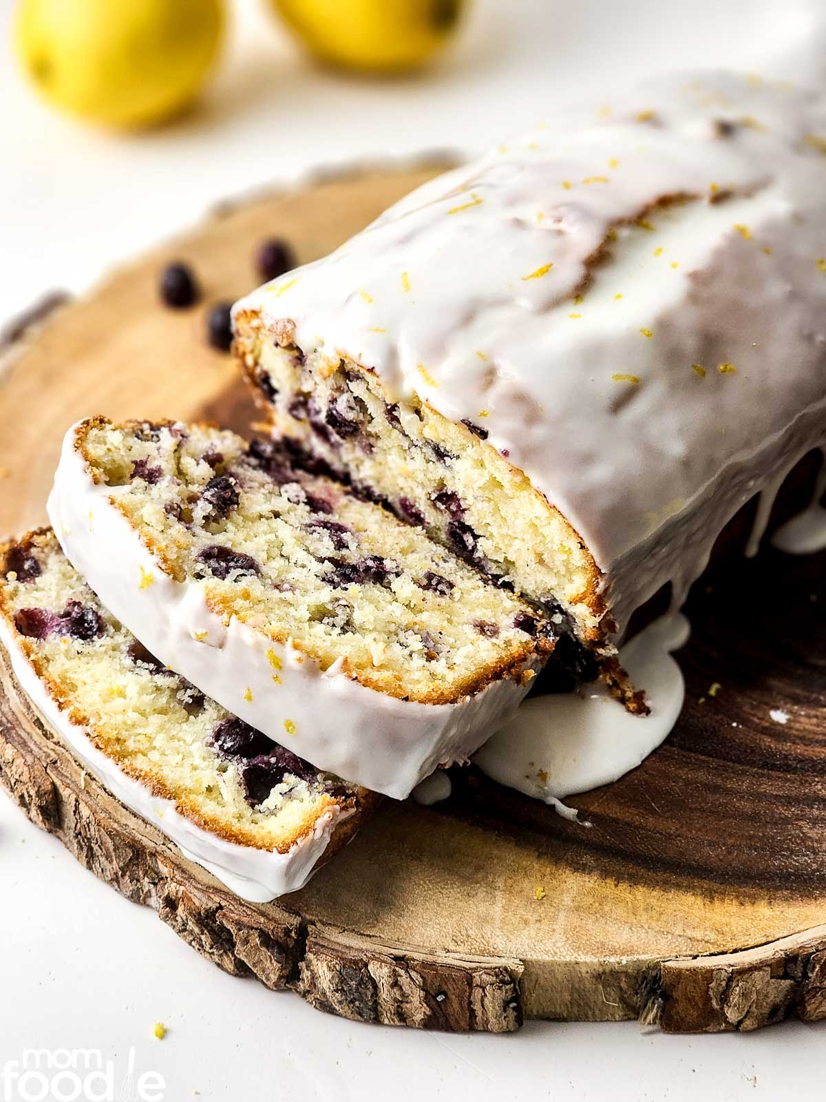 Lemon blueberry loaf cake with icing glaze and slices on a wooden board.