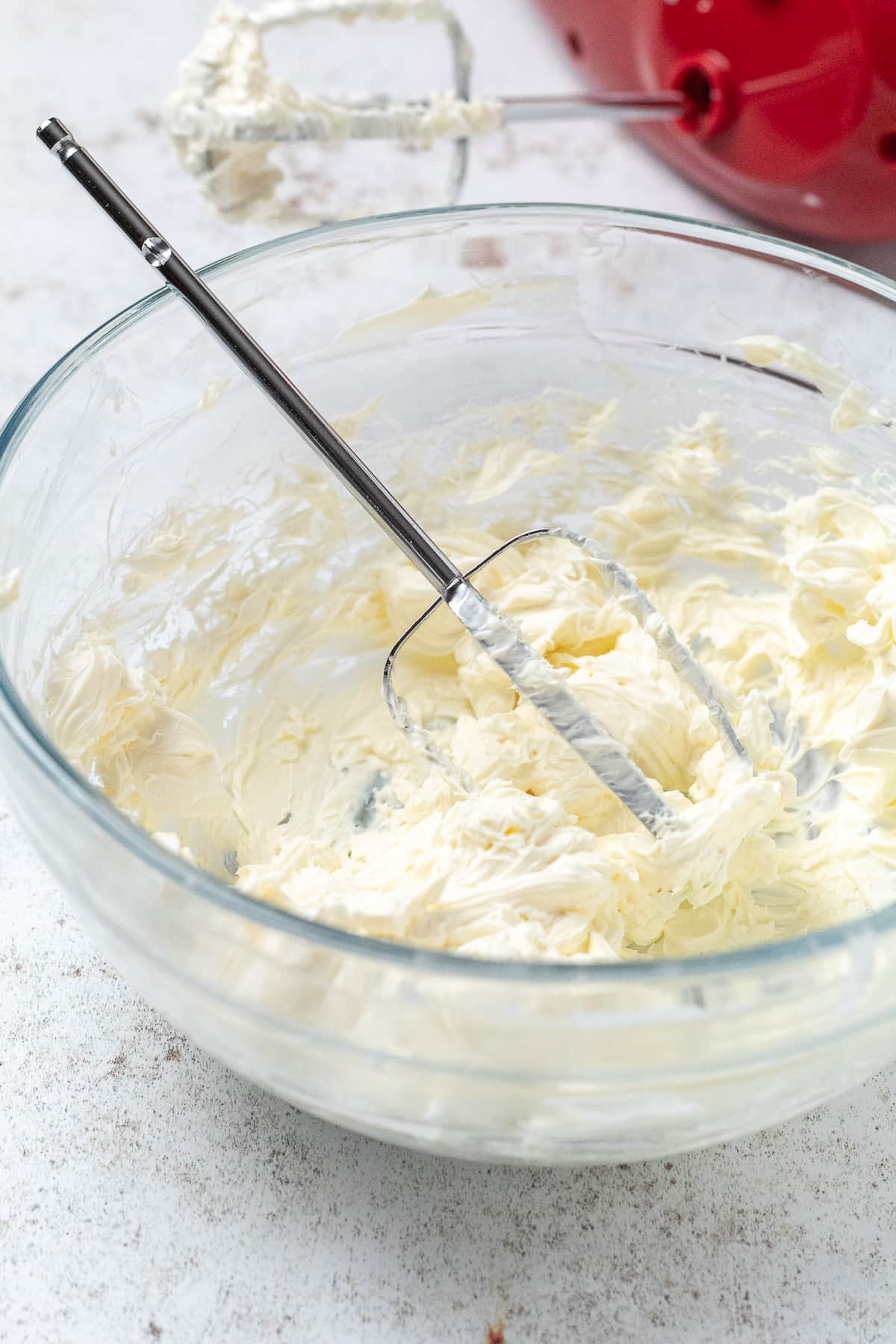 Cream cheese mixture being blended in bowl with hand mixer.
