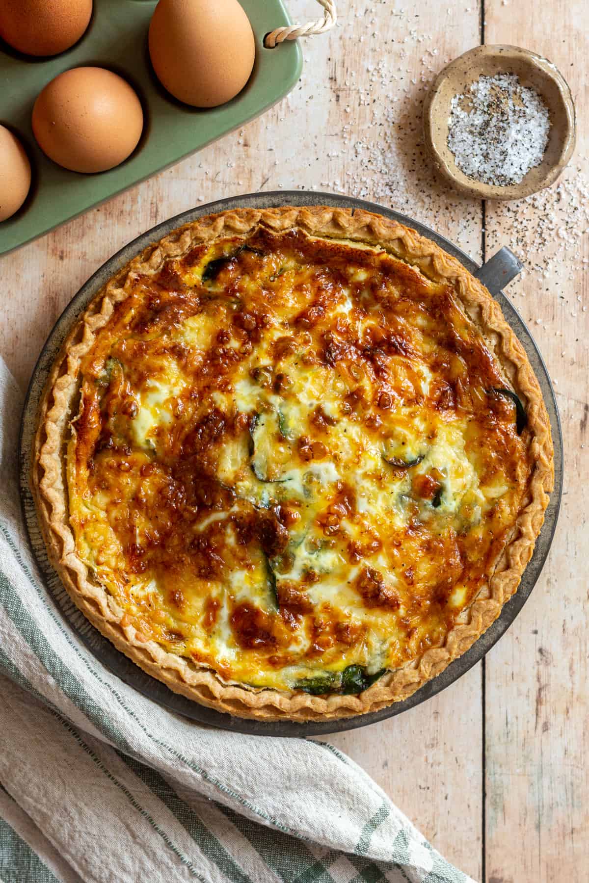 Golden spinach and sausage quiche in a flaky crust with eggs and seasoning on a rustic table.