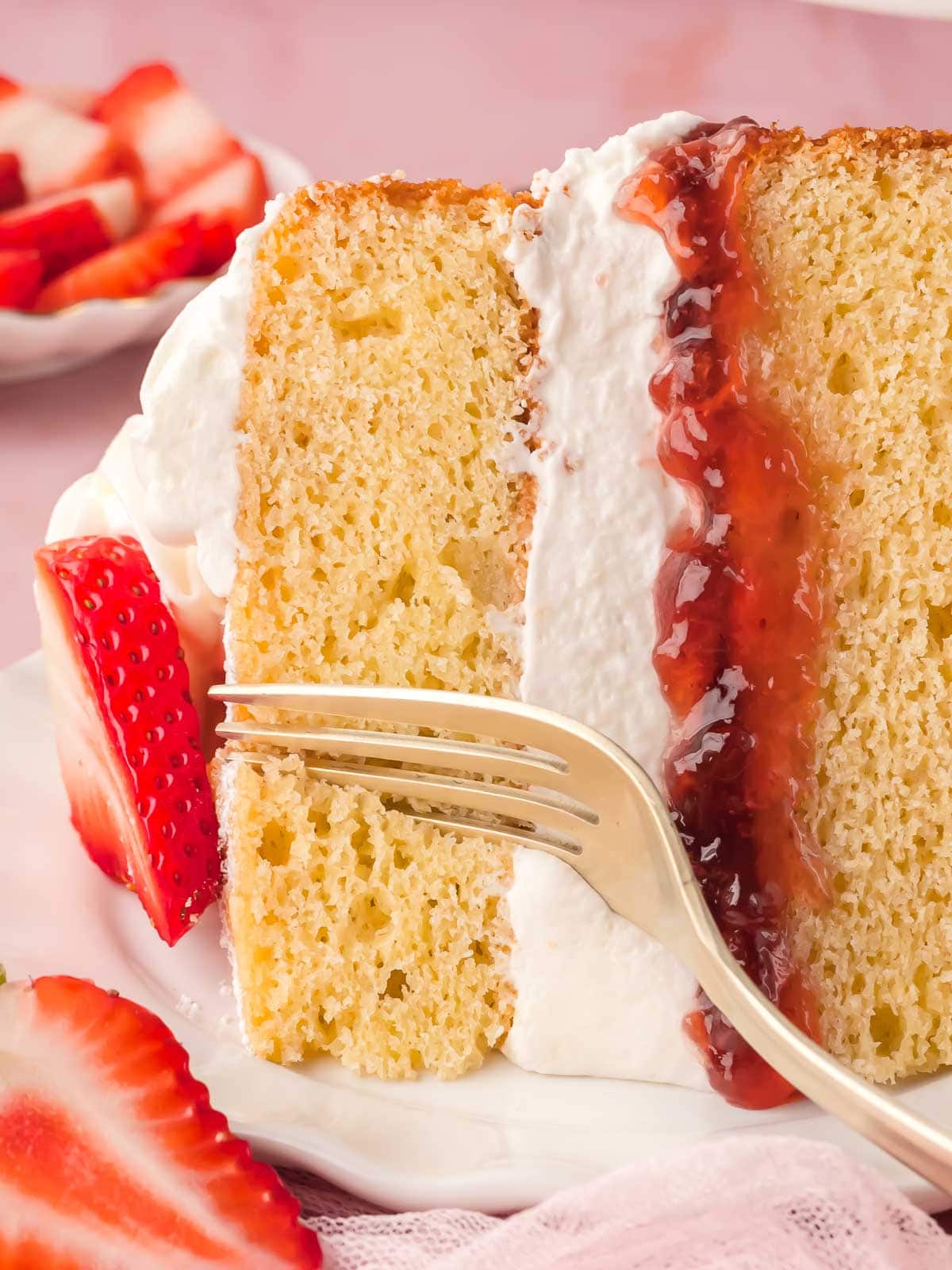 Victoria sponge cake slice with whipped cream and strawberry jam filling on a plate.