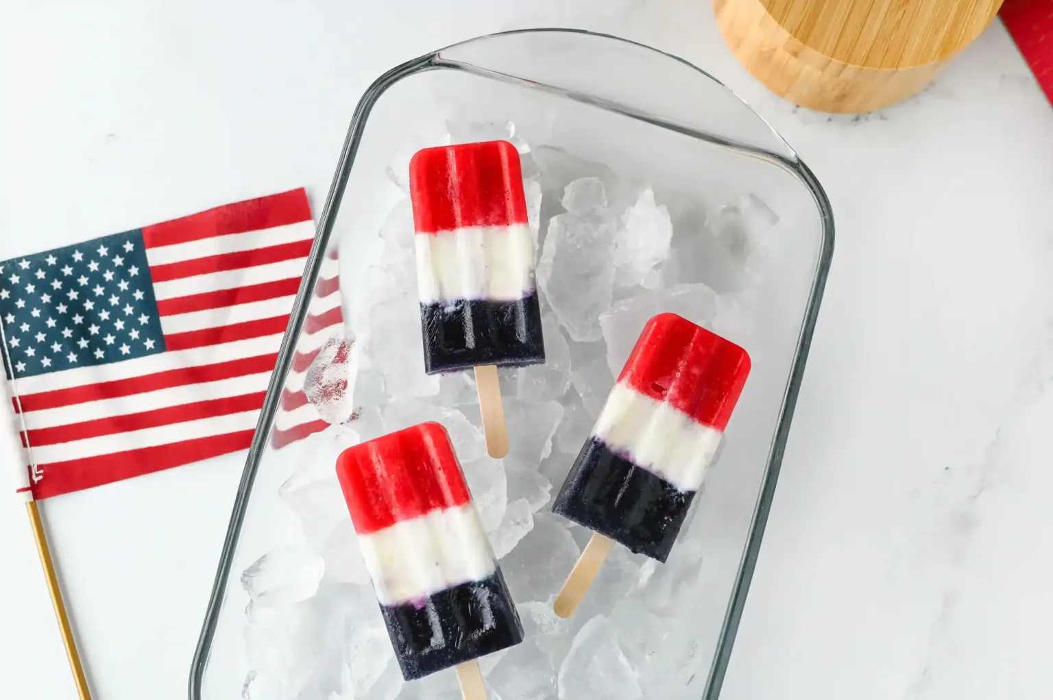 Red, white, and blue layered popsicles in ice with small American flag.