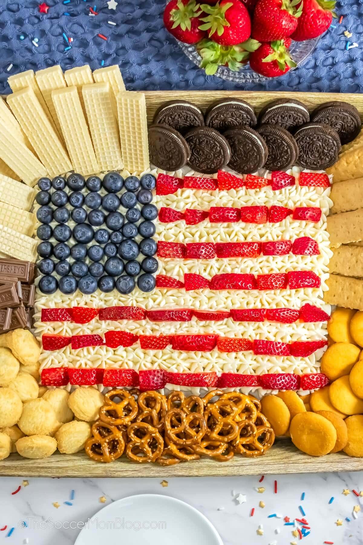 American flag dessert board with buttercream, strawberries, blueberries, cookies, and wafers.
