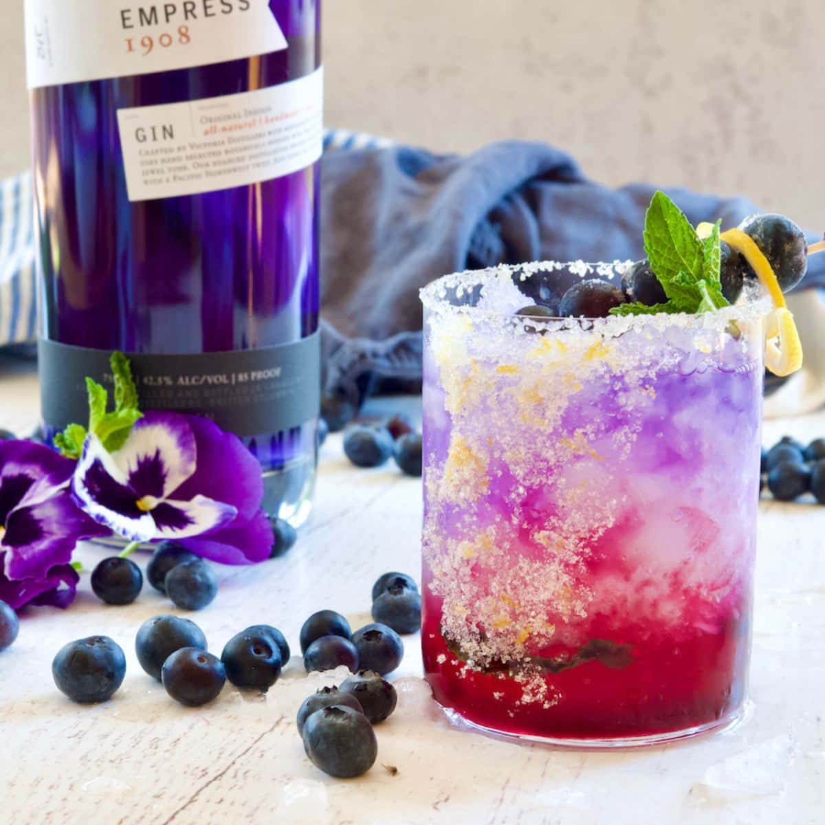 Blueberry gin cocktail with a sugar rim, fresh blueberries, and mint garnish.