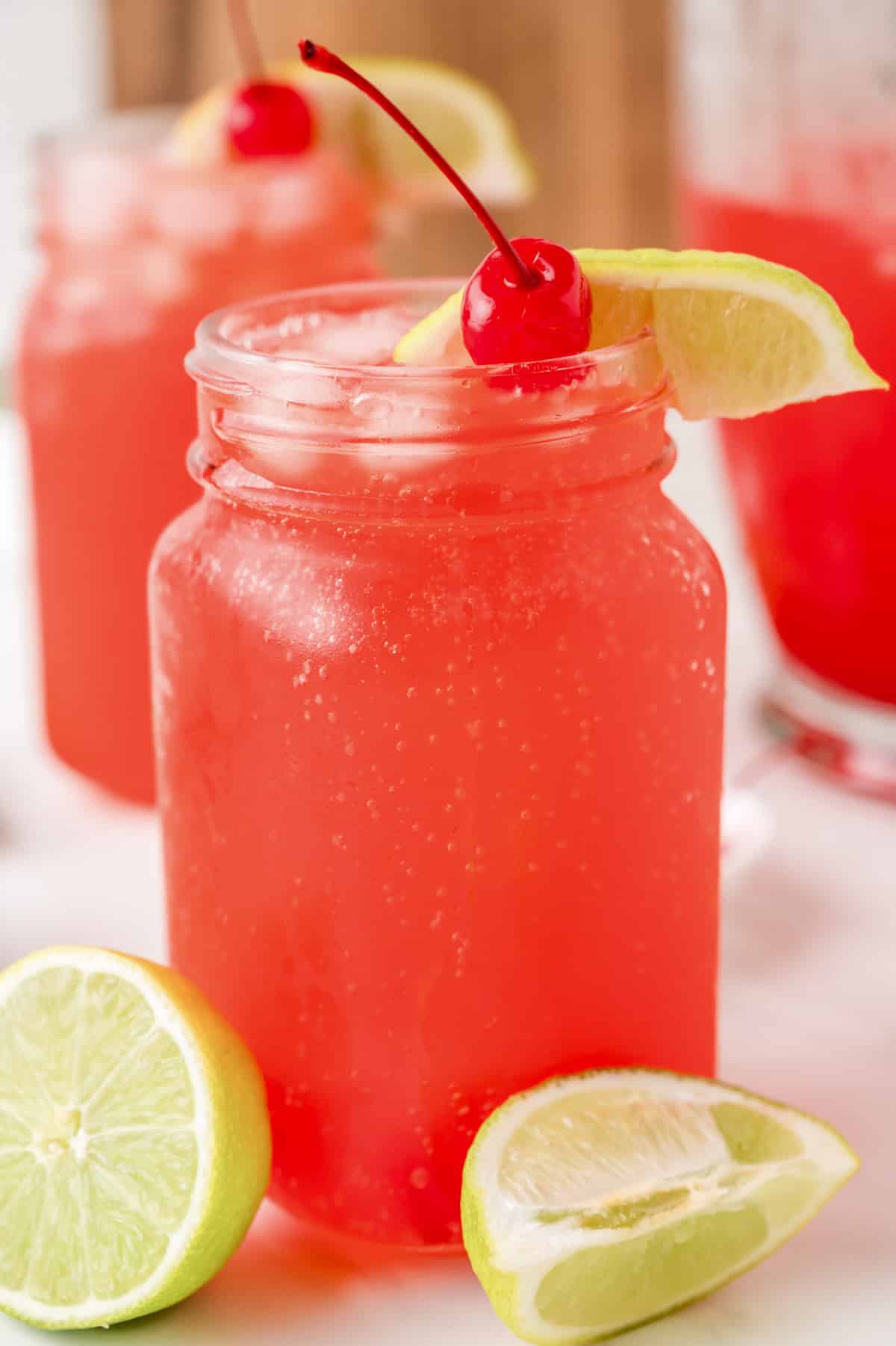Cherry limeade in a mason jar with ice, lime wedges, and a maraschino cherry garnish.