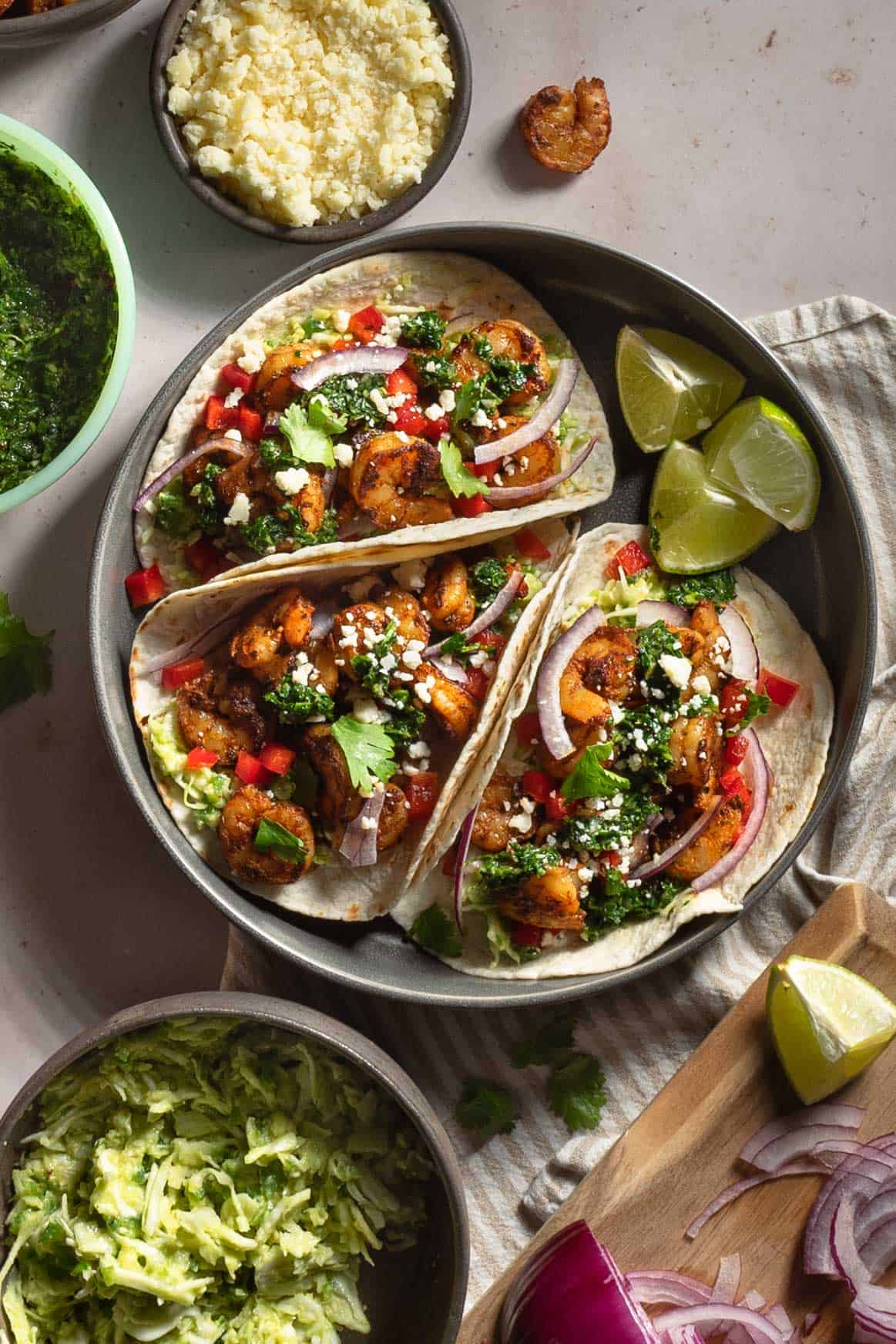 Shrimp tacos topped with chimichurri, red onion, and crumbled cheese.