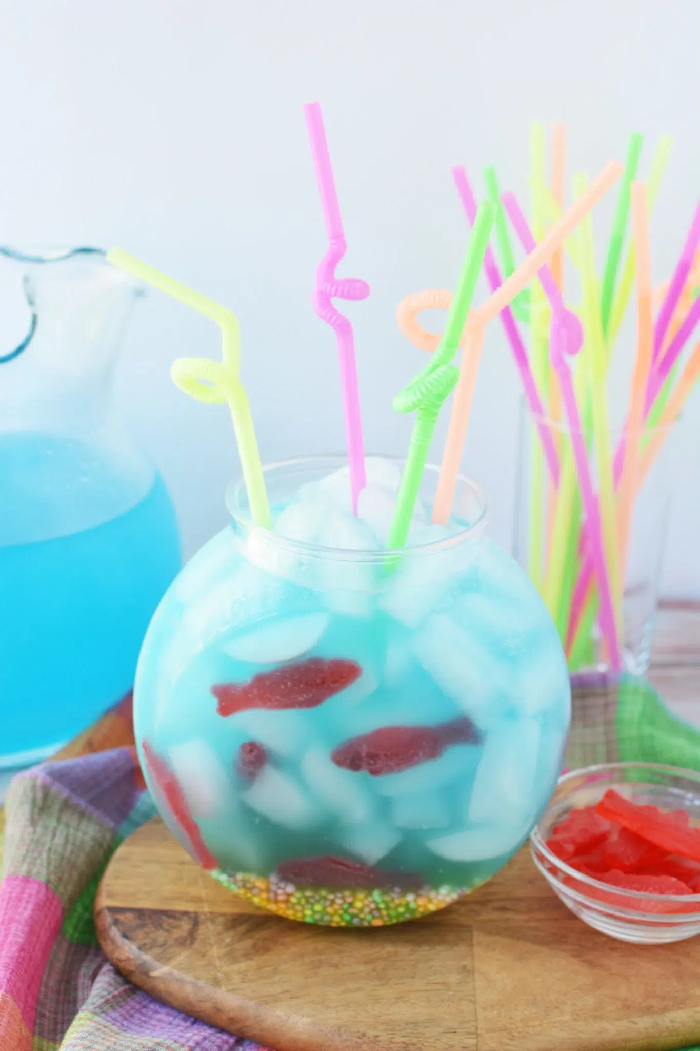 Blue fishbowl mocktail with ice, colorful bendy straws, and gummy fish candies.