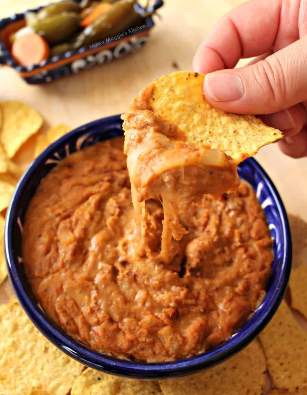 Frijoles puercos dip with melted cheese and tortilla chip scoop.