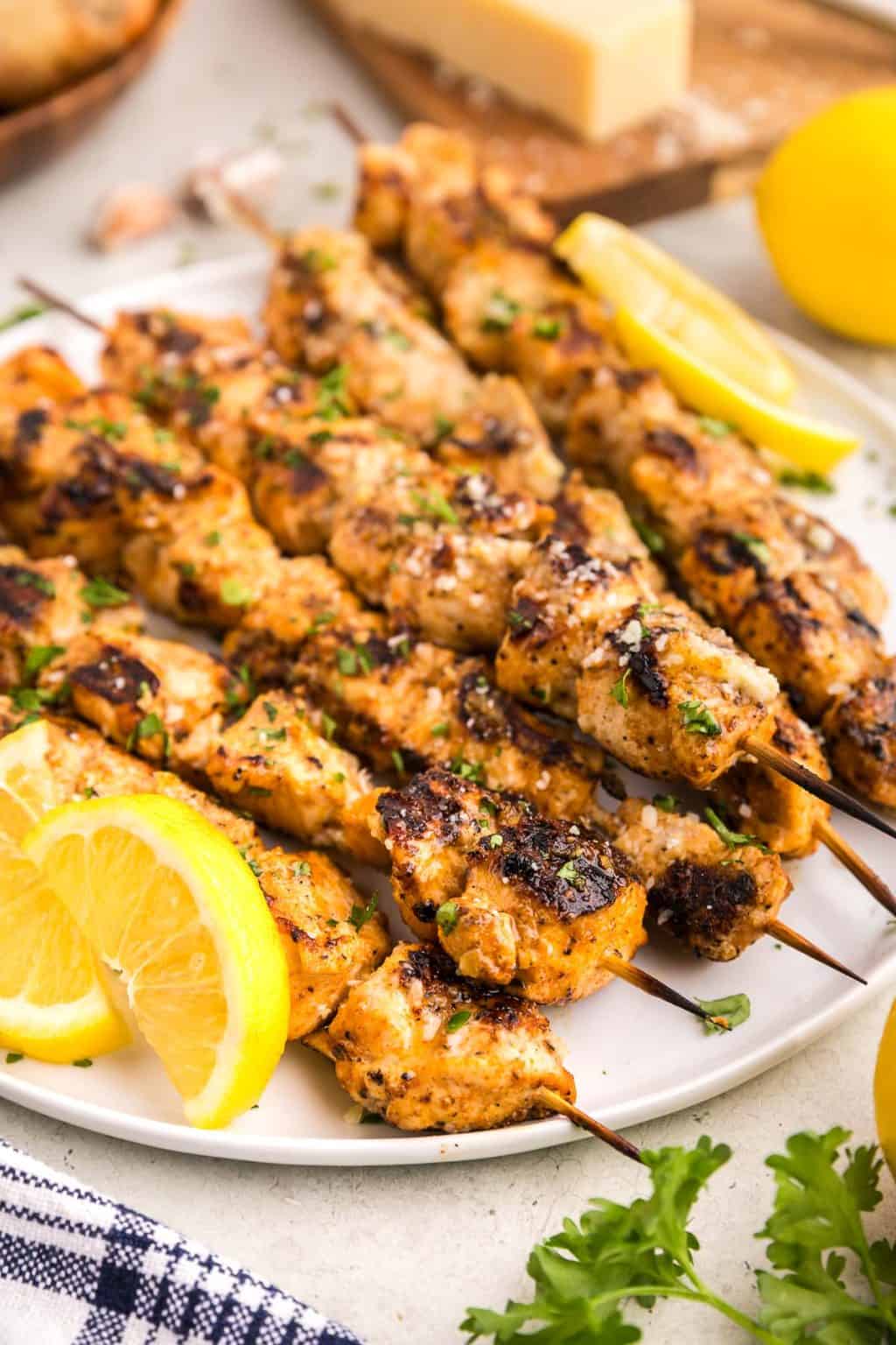 Grilled garlic parmesan chicken skewers with lemon wedges.