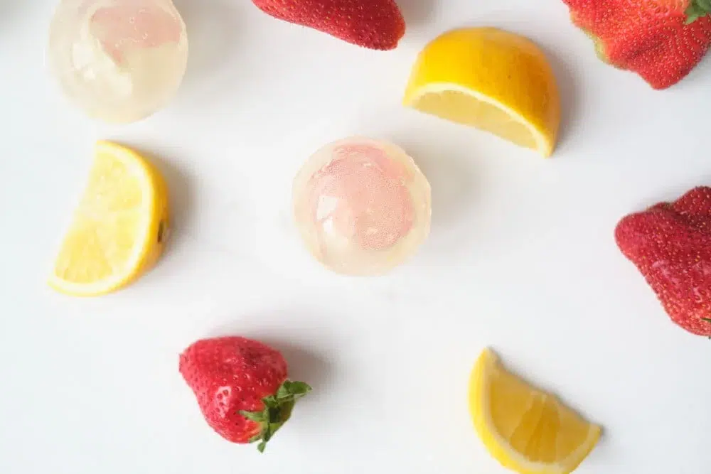 Small round lemon drink balls arranged with strawberries and lemon slices on white surface