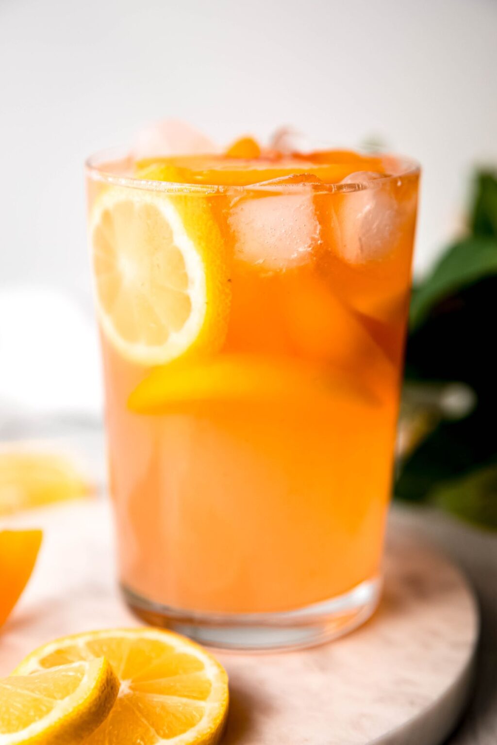 Glass of peach lemonade with ice and lemon slice on wooden board.