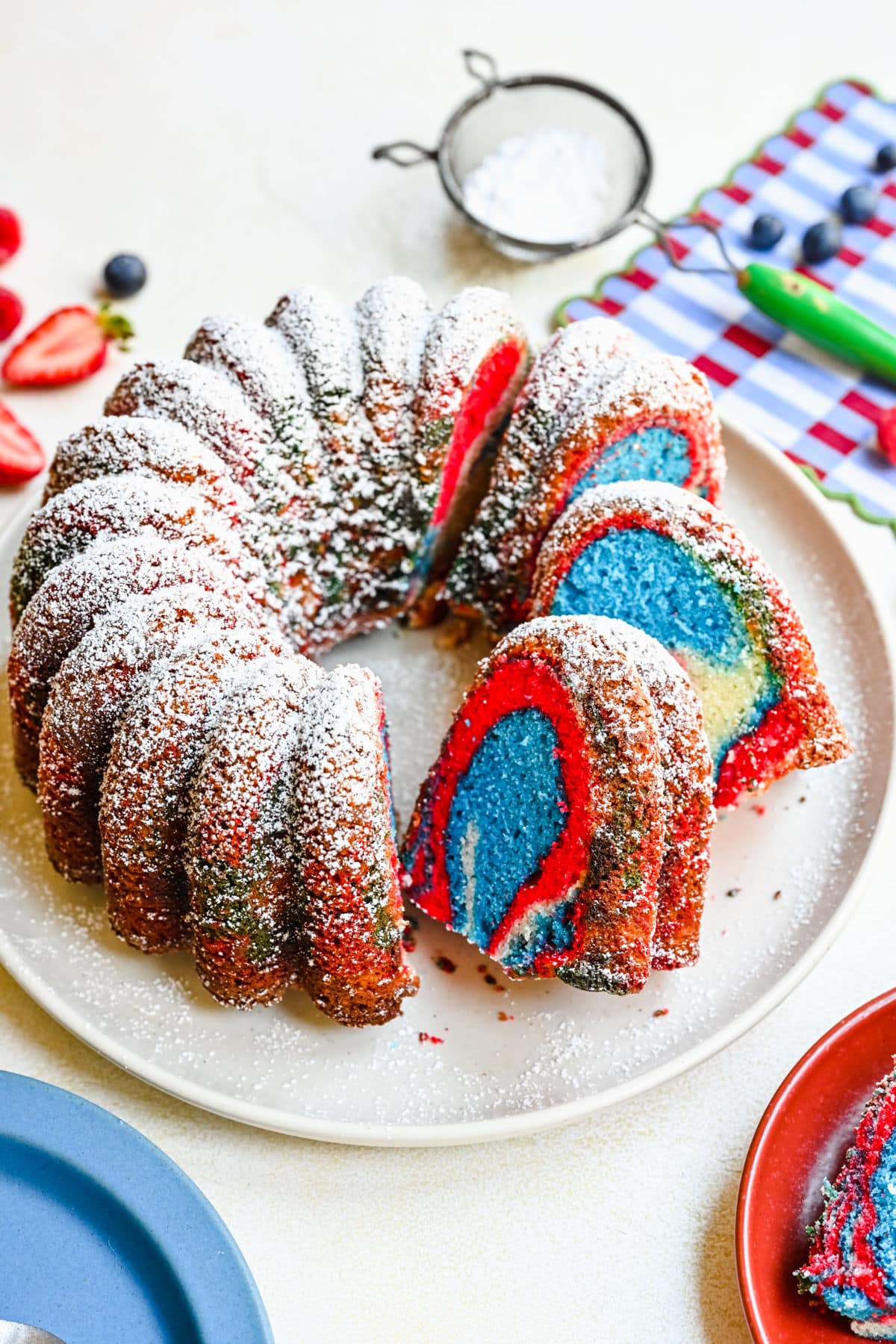 Patriotic bundt cake with red, white, and blue swirls dusted with powdered sugar, sliced to show layers.
