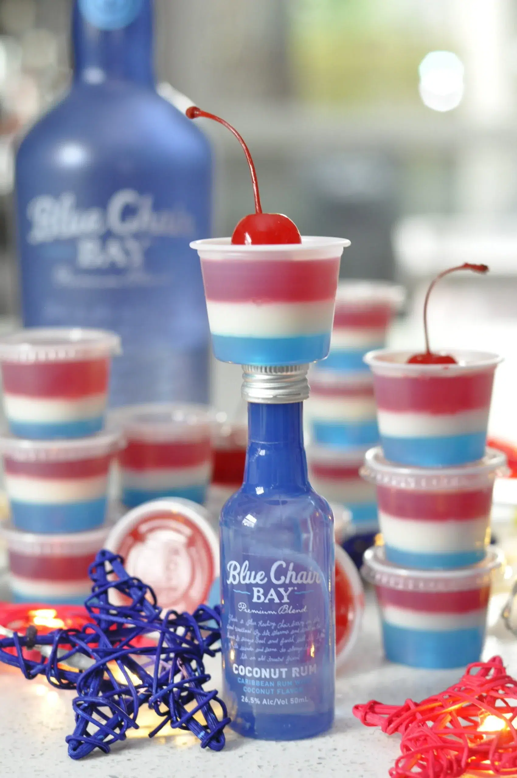 Red, white, and blue layered jello shots topped with cherries for a festive party.