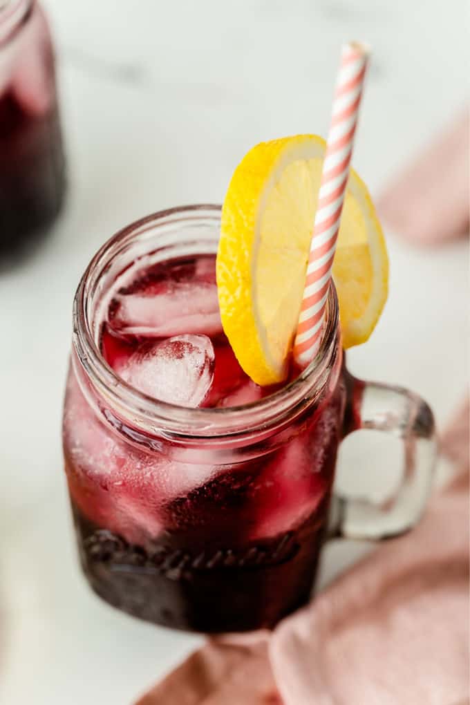 Two glasses of red lemonade with lemon slices on a light surface.