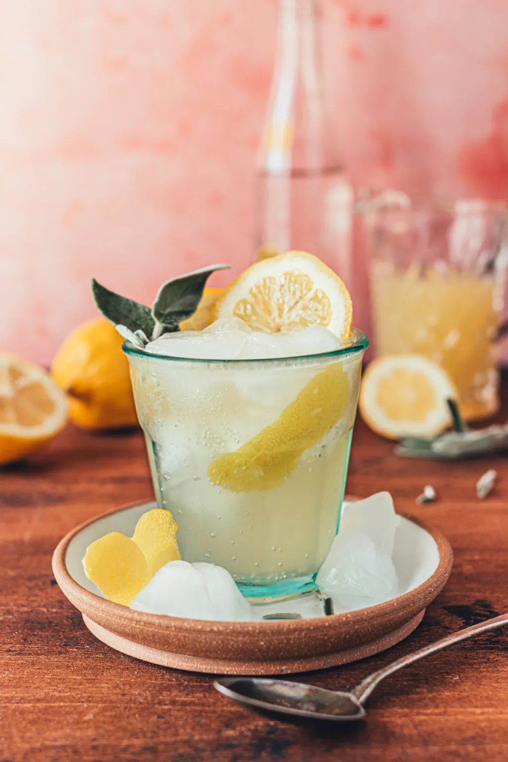 Glass of sparkling sage lemonade with ice and lemon peel on a saucer.
