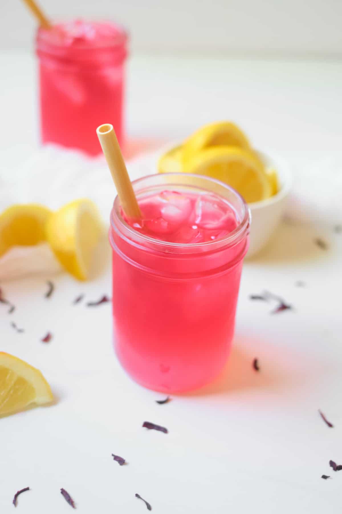 Glass jar of pink lemonade with ice and striped straw, lemon slices in background.