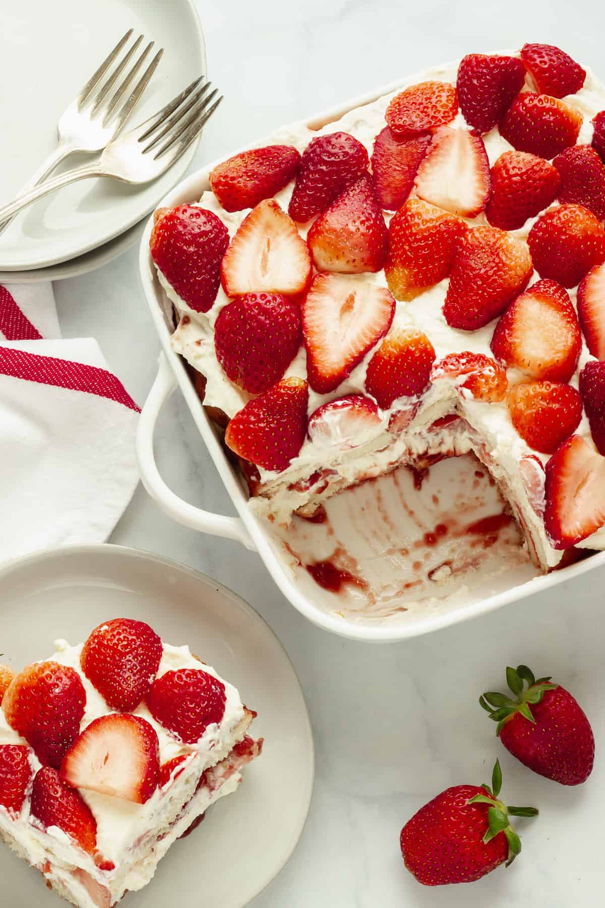 Strawberry tiramisu with layers of cream and strawberries in dish, partially served.
