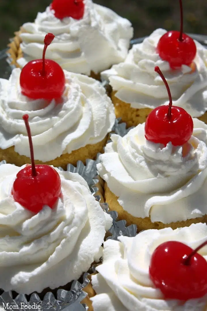 Tres leches cupcakes topped with whipped cream frosting and maraschino cherries.