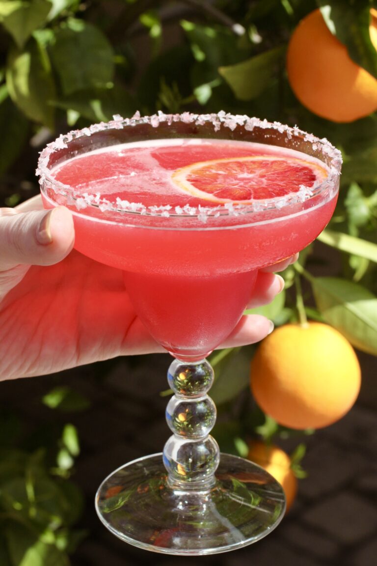 Blood orange margarita on the rocks with salted rim and citrus slice.