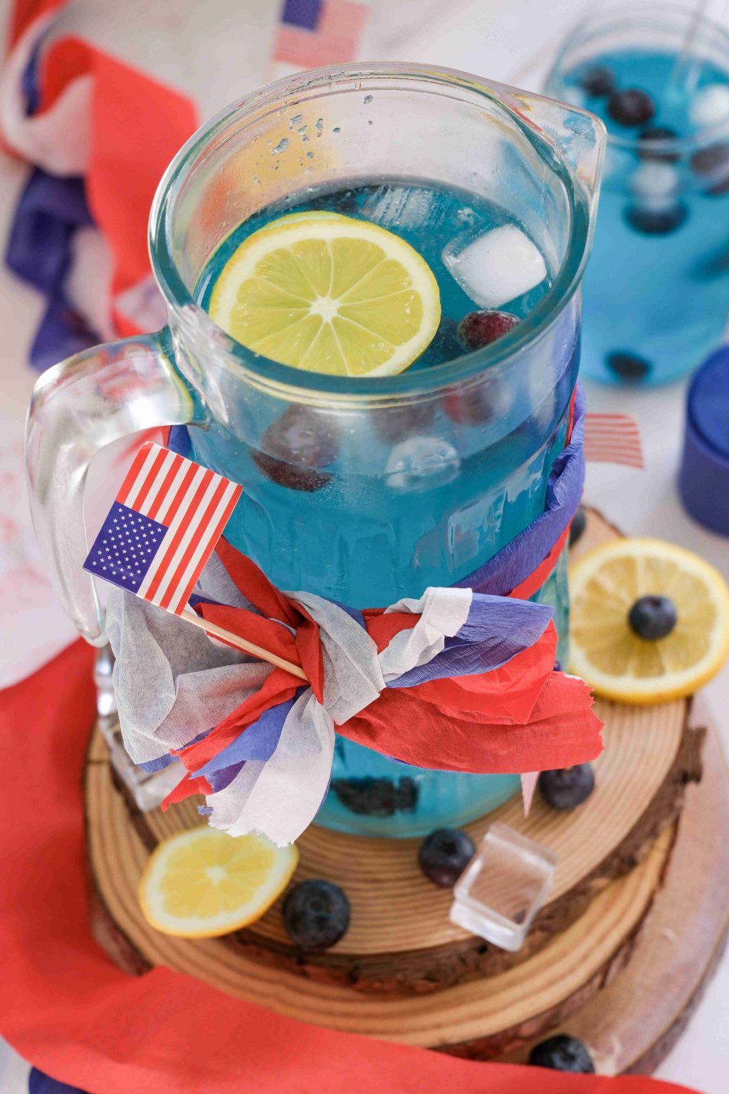 Blue lemonade in a glass pitcher with lemon slices and ice.
