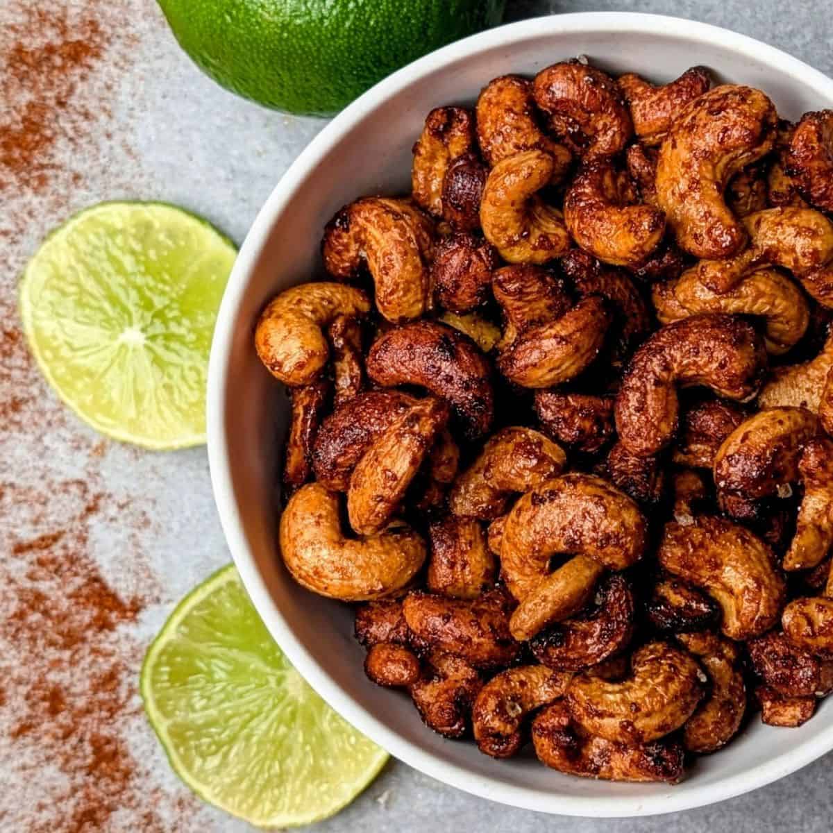 Chili lime roasted cashews in a bowl with fresh lime halves nearby.