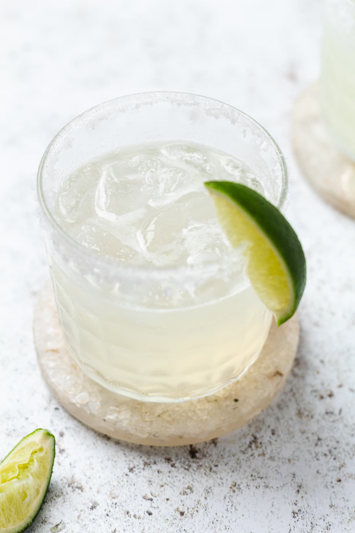 Classic margarita on the rocks in a salt-rimmed glass with a lime wedge, set on a light surface.