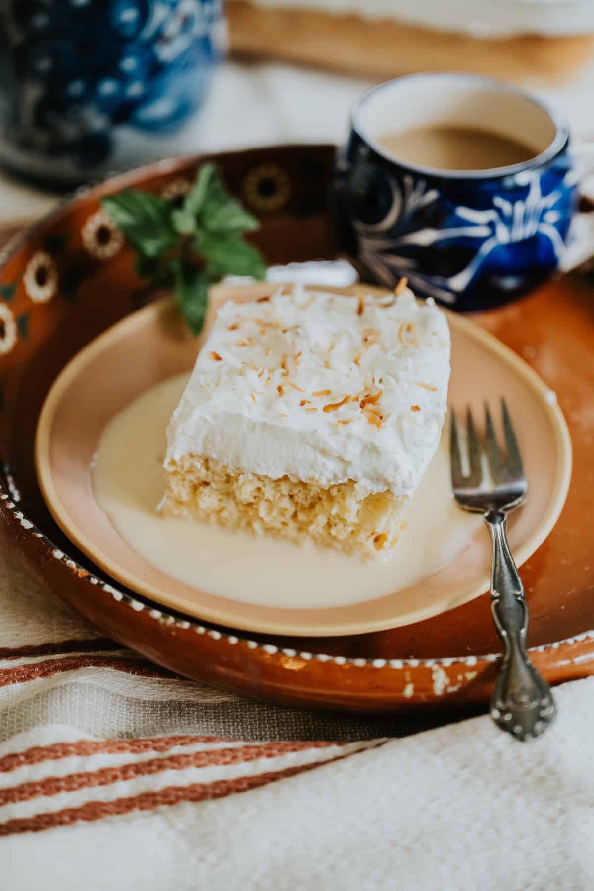 Slice of tres leches cake topped with whipped cream on a plate.