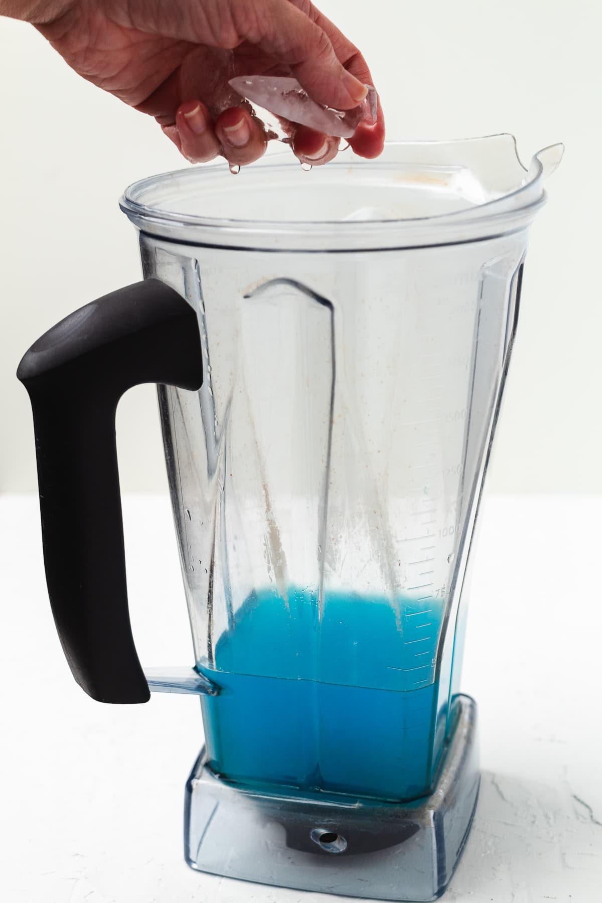 Hand adding ice to a pitcher with margarita ingredients.