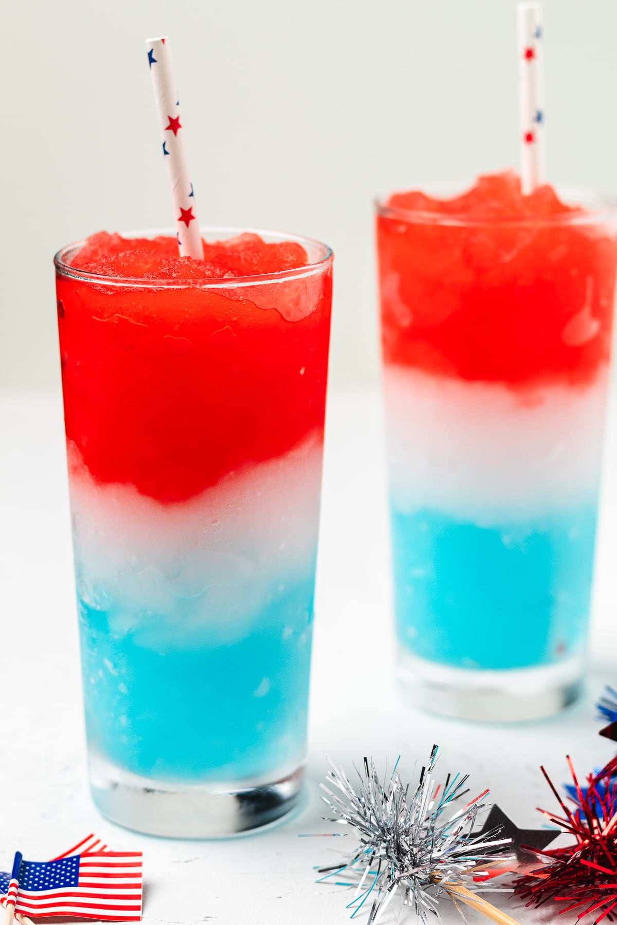 Frozen red, white, and blue layered margaritas in tall glasses with patriotic straws.