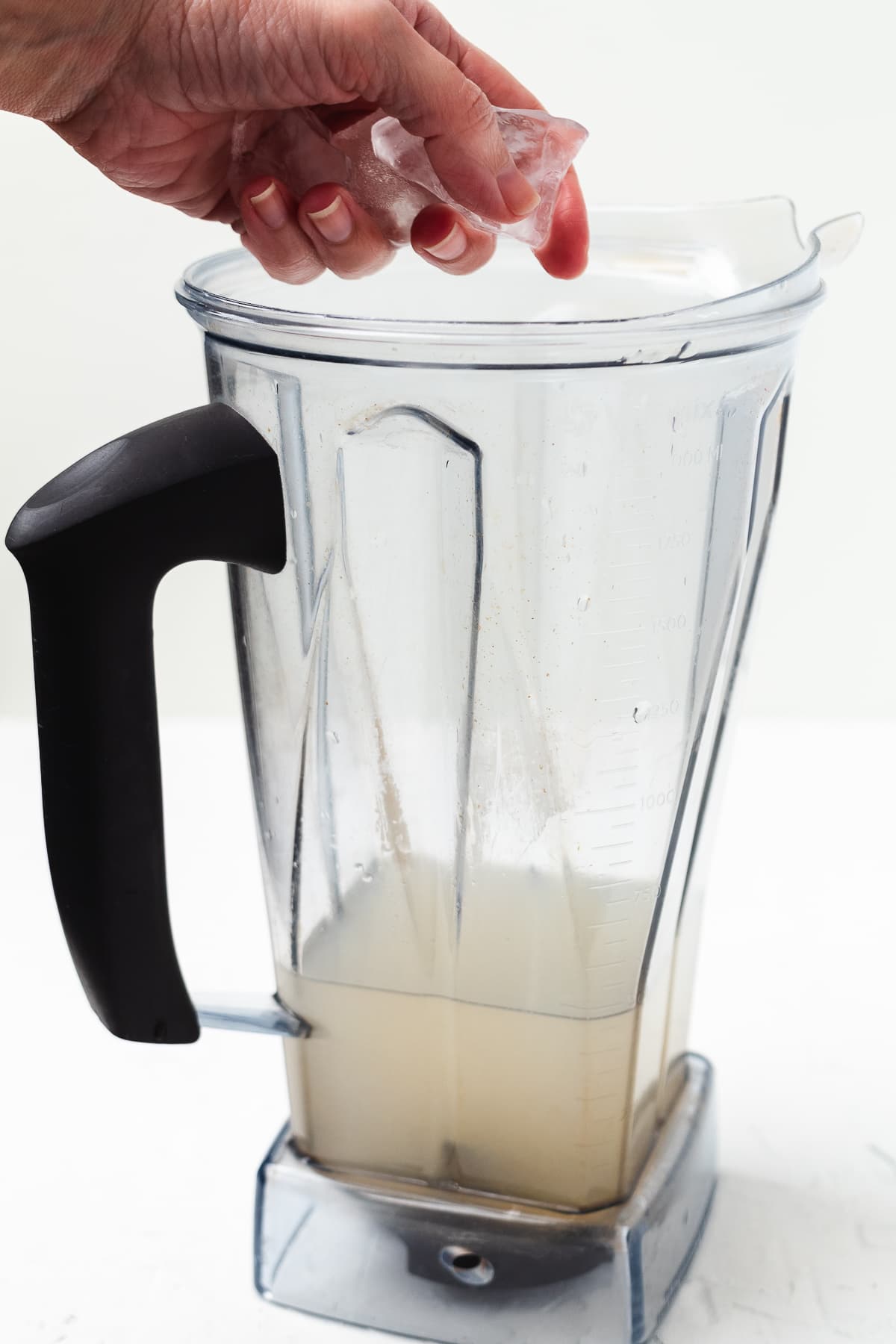 Hand adding ice to a pitcher with white margarita ingredients.