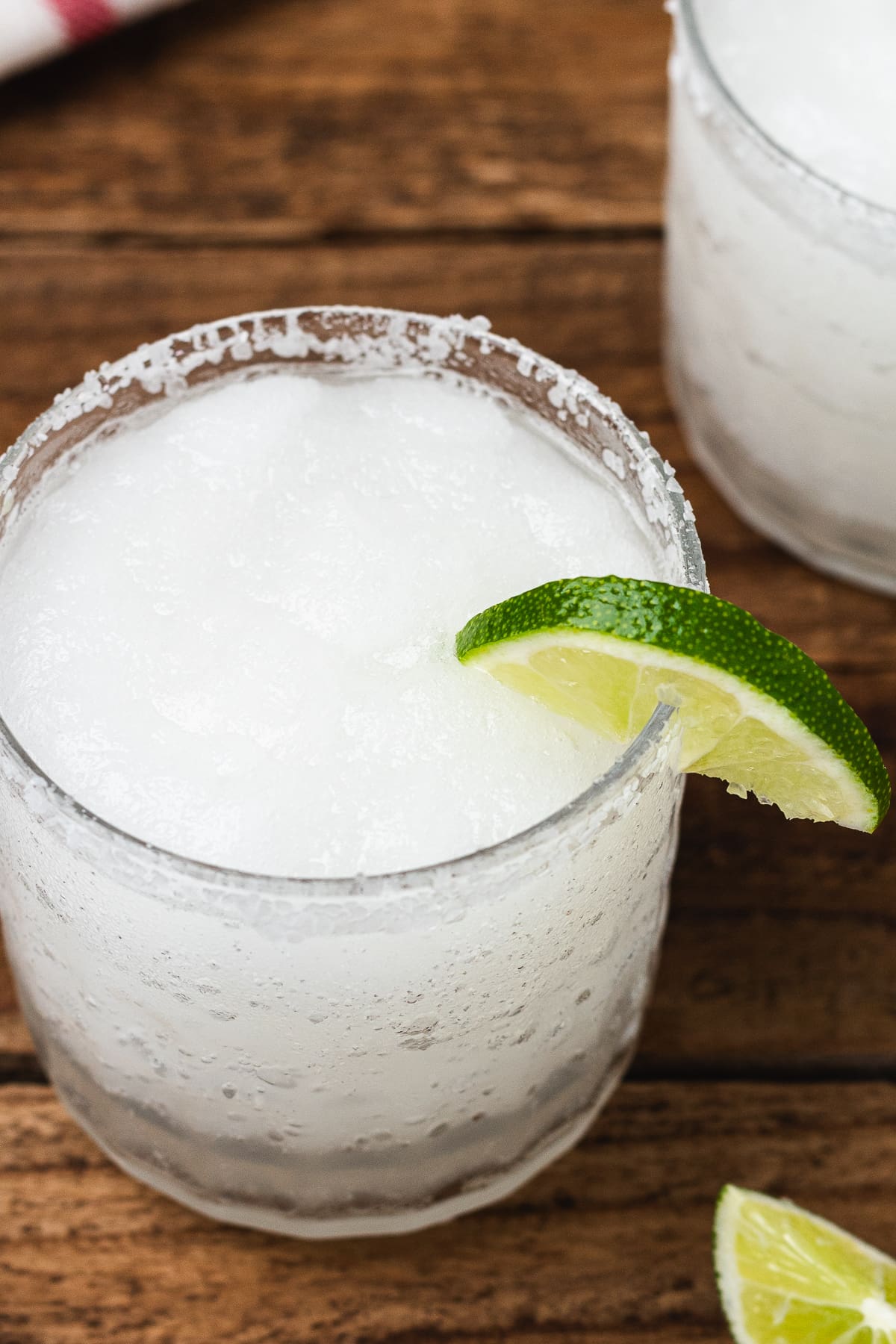 Frozen white margarita with a salted rim and lime wedge on a wooden table.