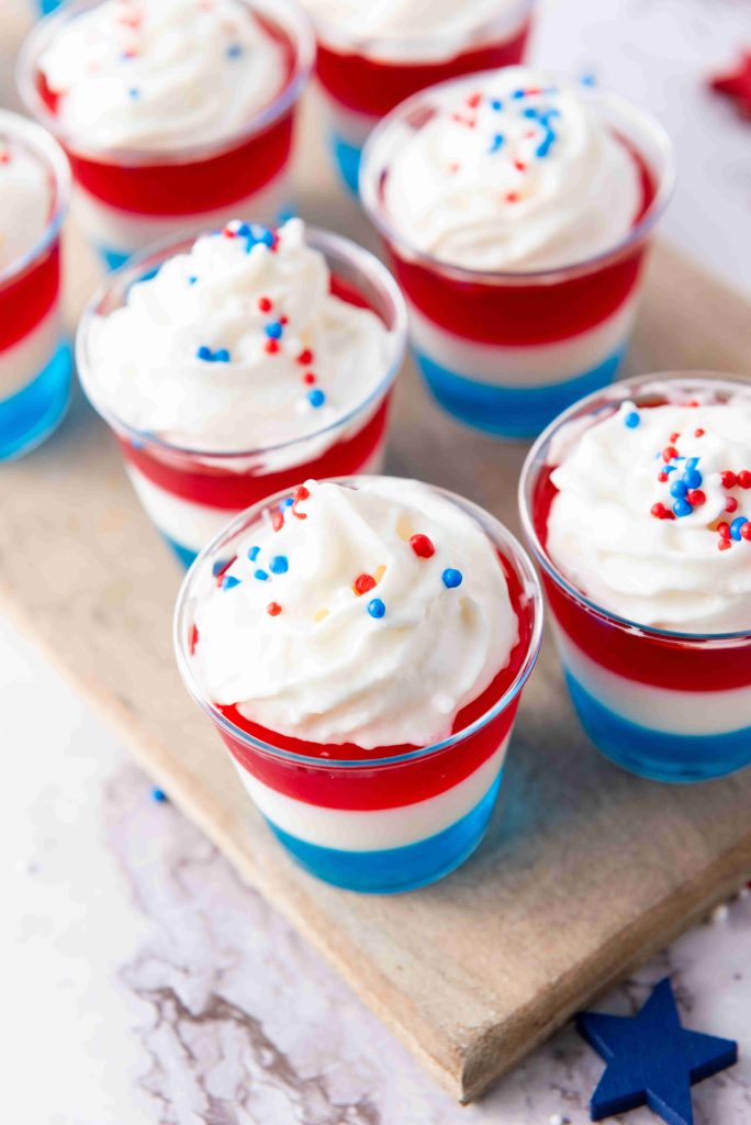 Red, white, and blue layered jello cups topped with whipped cream and sprinkles.